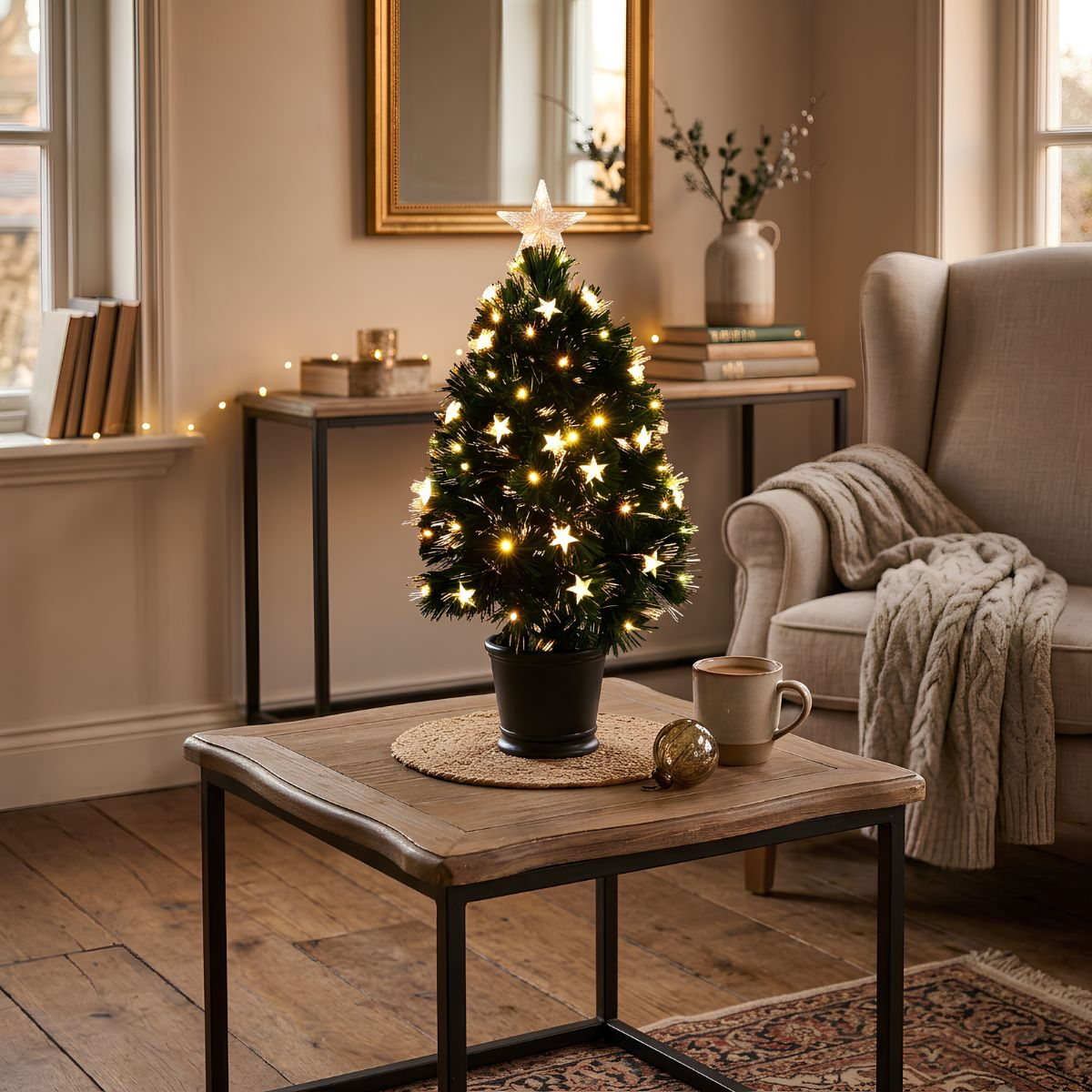 Ein beleuchteter Tisch-Weihnachtsbaum mit Sternenlicht steht auf einem Holztisch neben einer Tasse und einem Sessel.