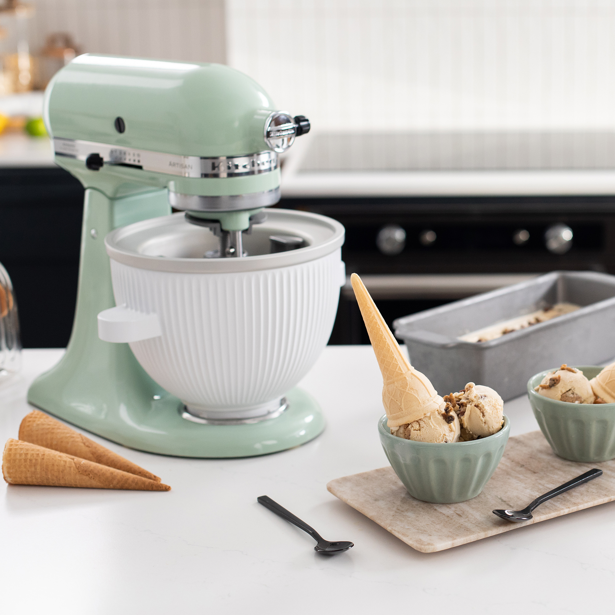Un'impastatrice verde menta con ciotola per gelato, coni e gelato nelle ciotole su un bancone.