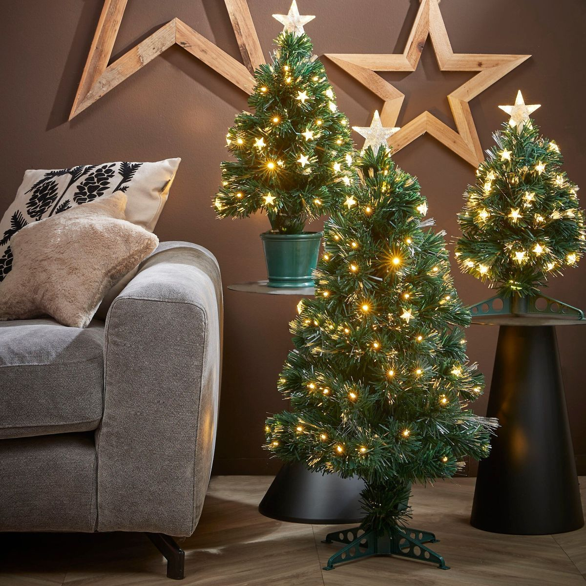 Three small lighted Christmas trees stand in a living room in front of a wall with wooden stars.