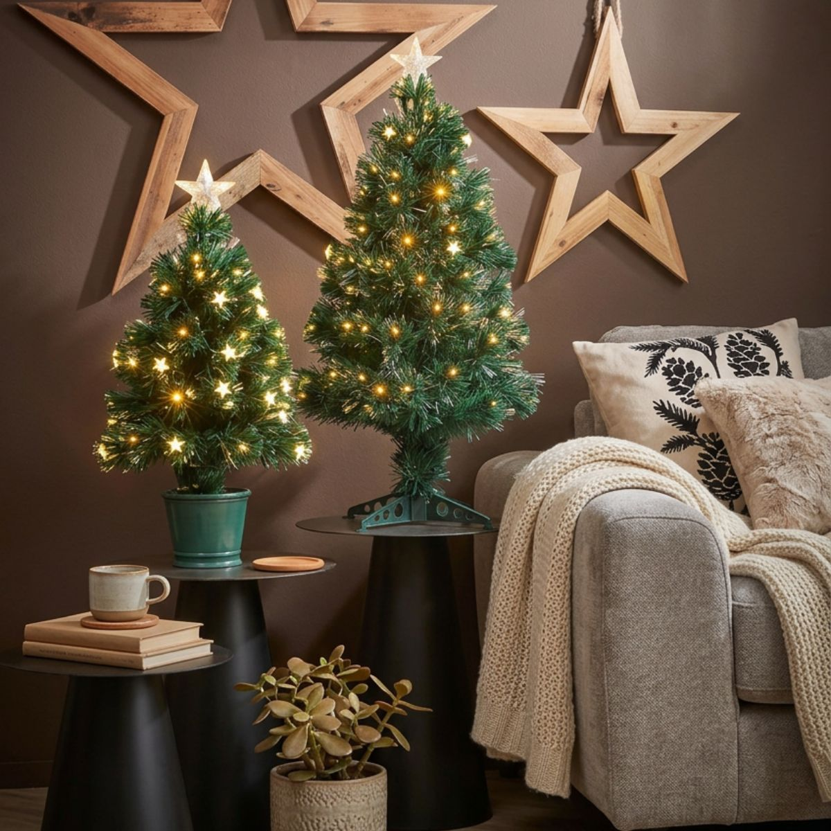 Two lit tabletop Christmas trees on stands next to a sofa with wooden star wall decor and a plant.