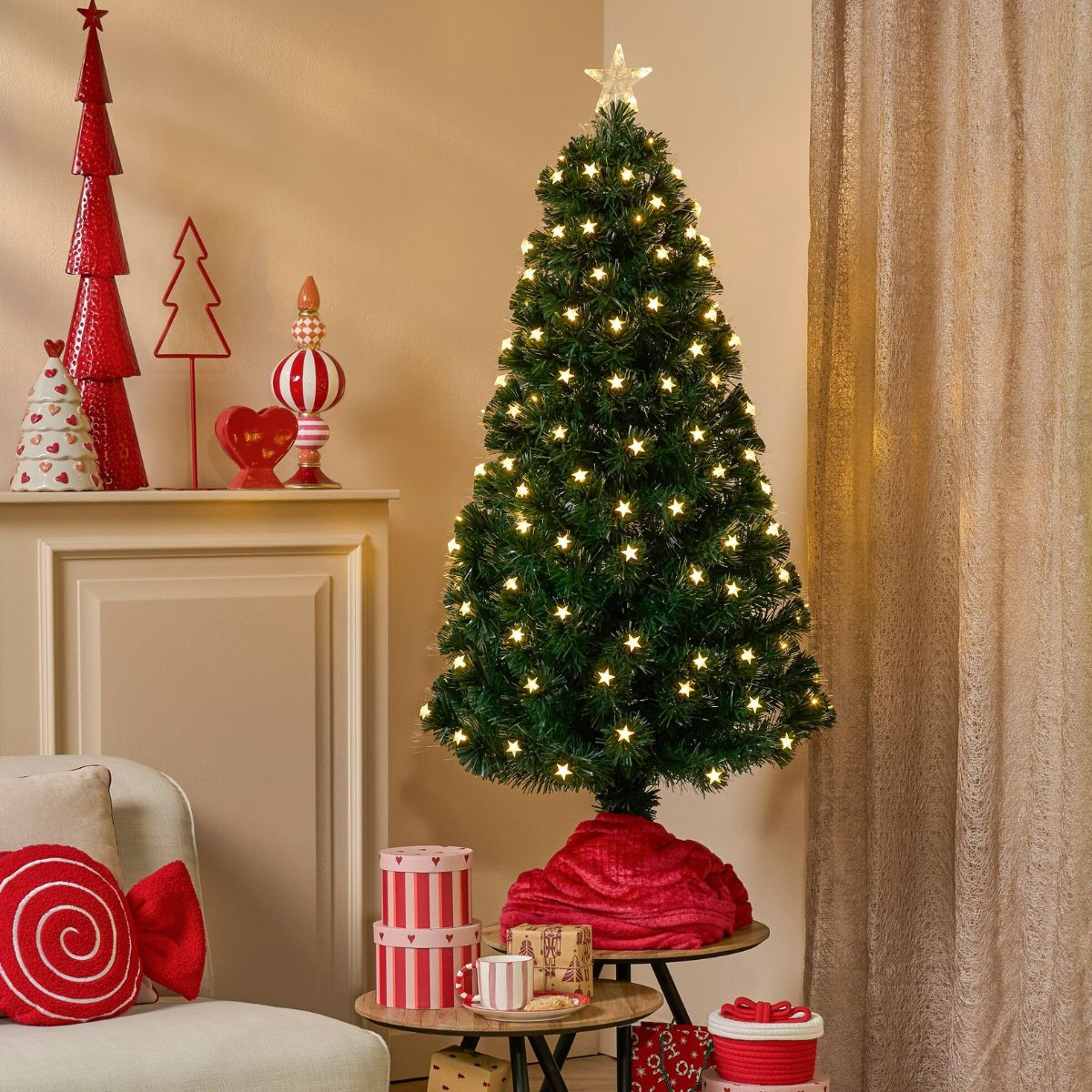 Decorated Christmas tree with lights, red decorations on a cabinet, and gifts underneath it in a room.