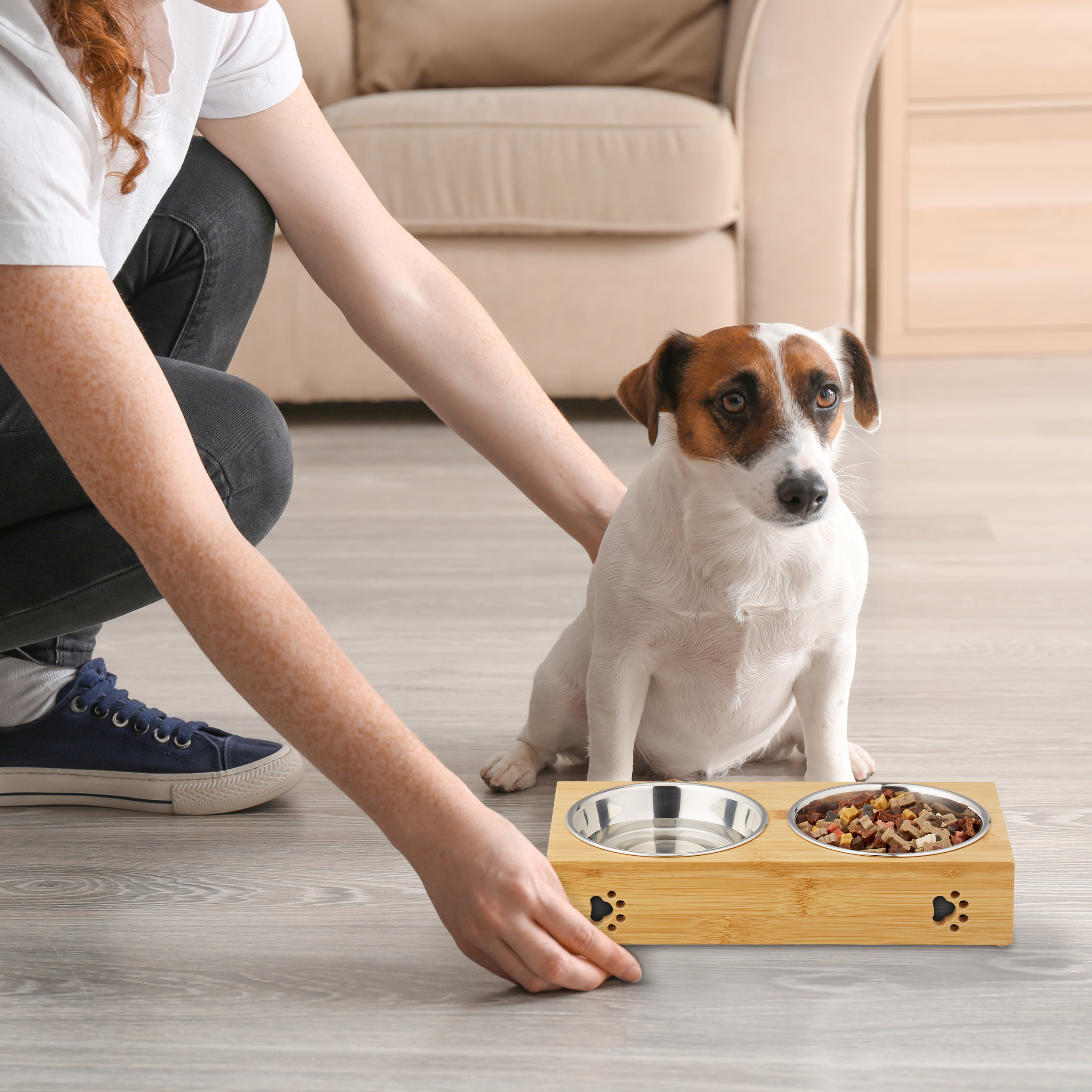 Eine Frau stellt einen doppelten Futternapf aus Holz mit Wasser und Futter für einen Jack Russell Terrier hin.