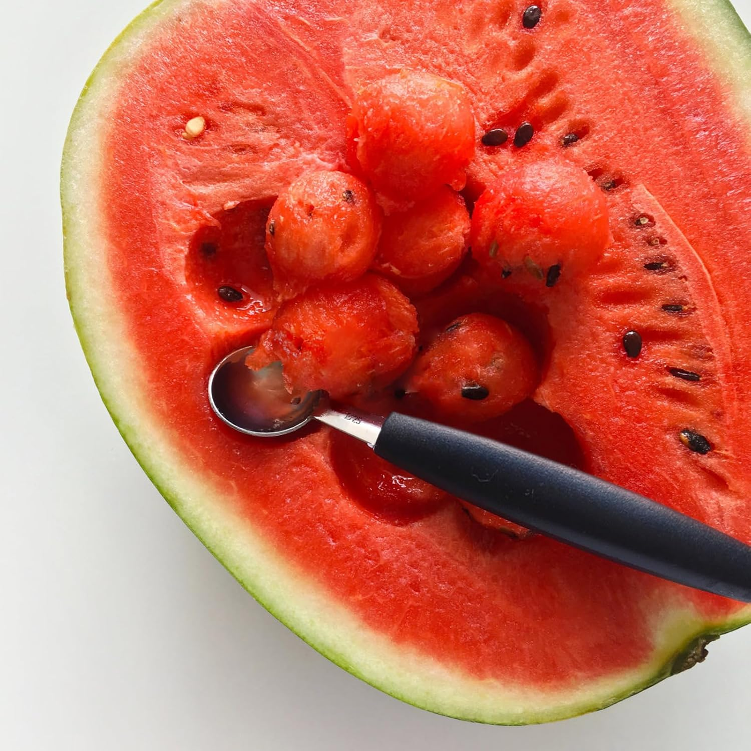 Ein Kugelausstecher holt runde Bällchen aus einer halbierten roten Wassermelone.