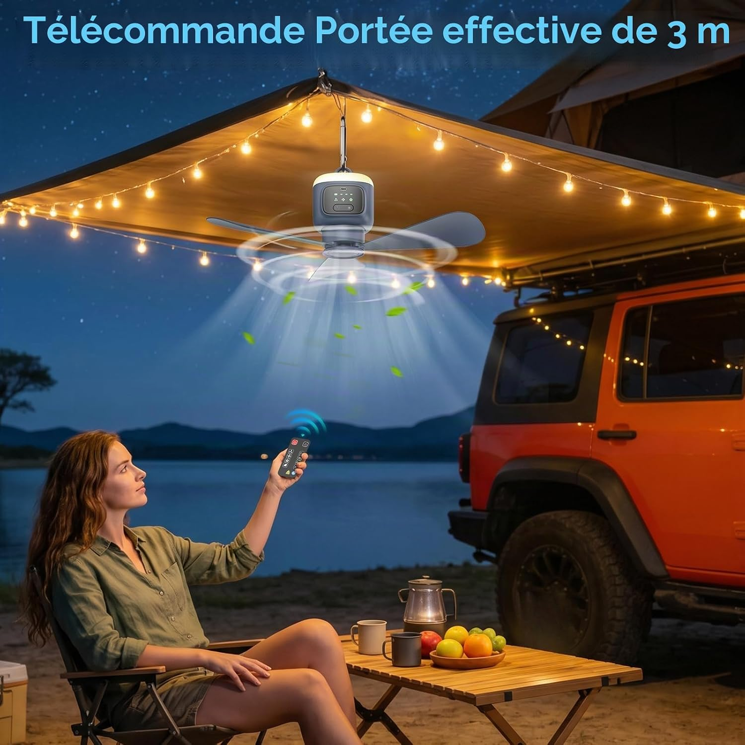Eine Frau sitzt nachts vor einem Wohnmobil, bedient mit einer Fernbedienung einen Camping-Deckenventilator unter einer Markise.