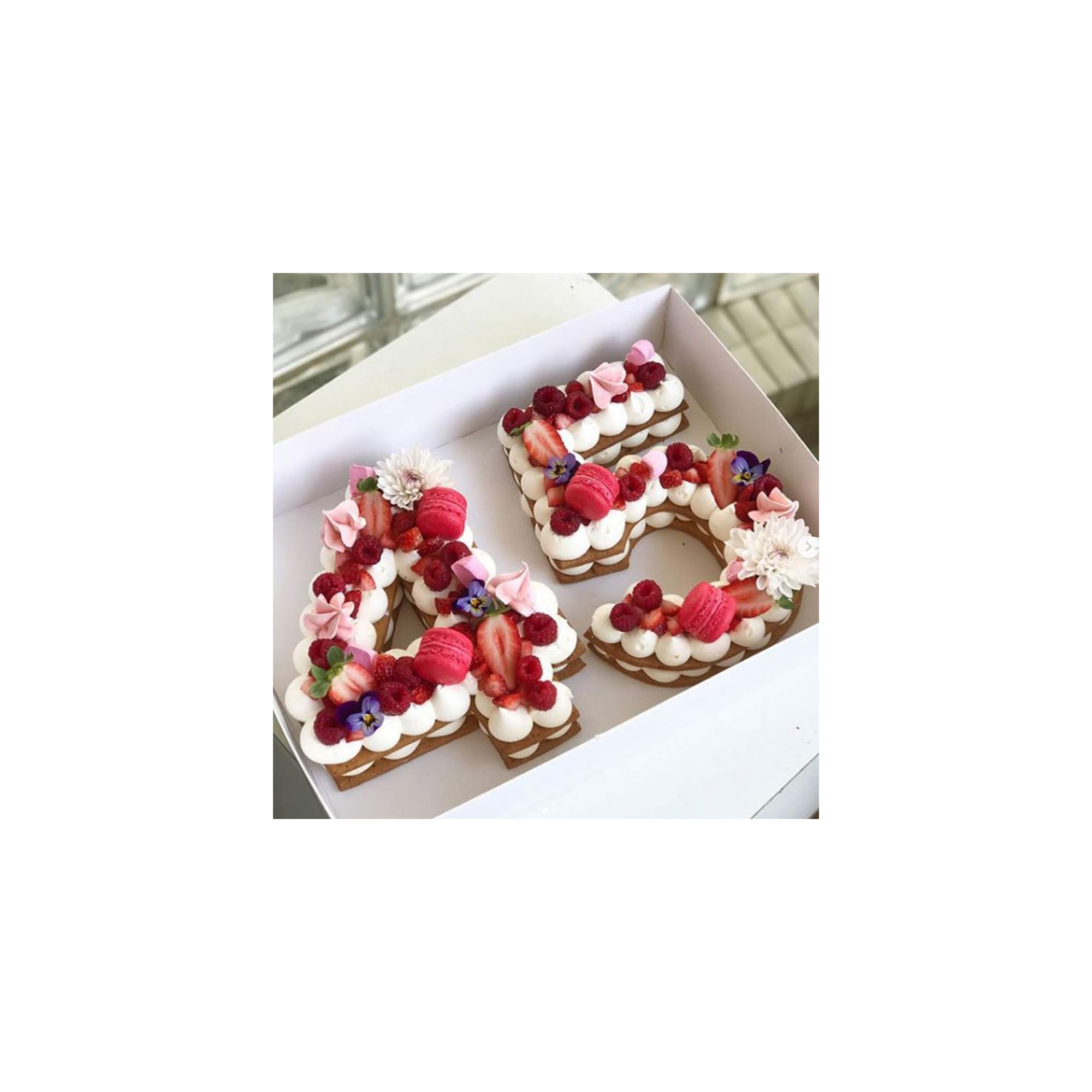 Zwei kuchen in Form der Zahlen 45, garniert mit weißer Creme, Himbeeren, Erdbeeren, Macarons und Blüten in einer Box.