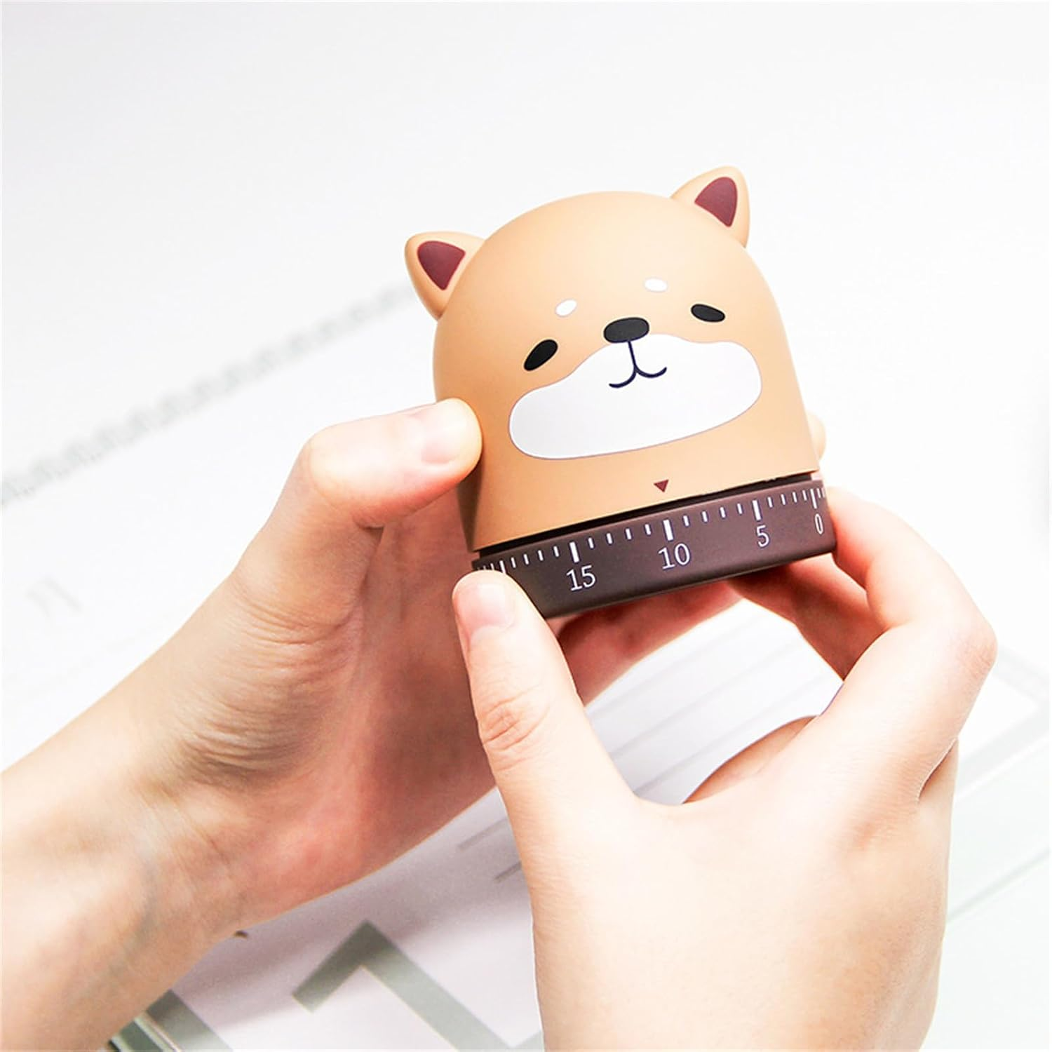 Ein Paar Hände hält einen niedlichen, braunen Shiba Inu Timer mit Zahlen an der Unterseite gegen einen hellen Hintergrund.