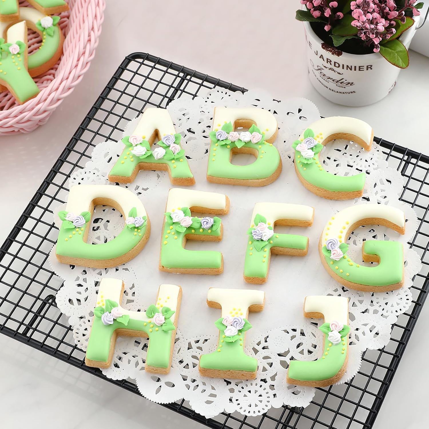 Alphabetkekse A bis J, verziert mit grünem Zuckerguss und kleinen Blumen, auf einem Gitter.
