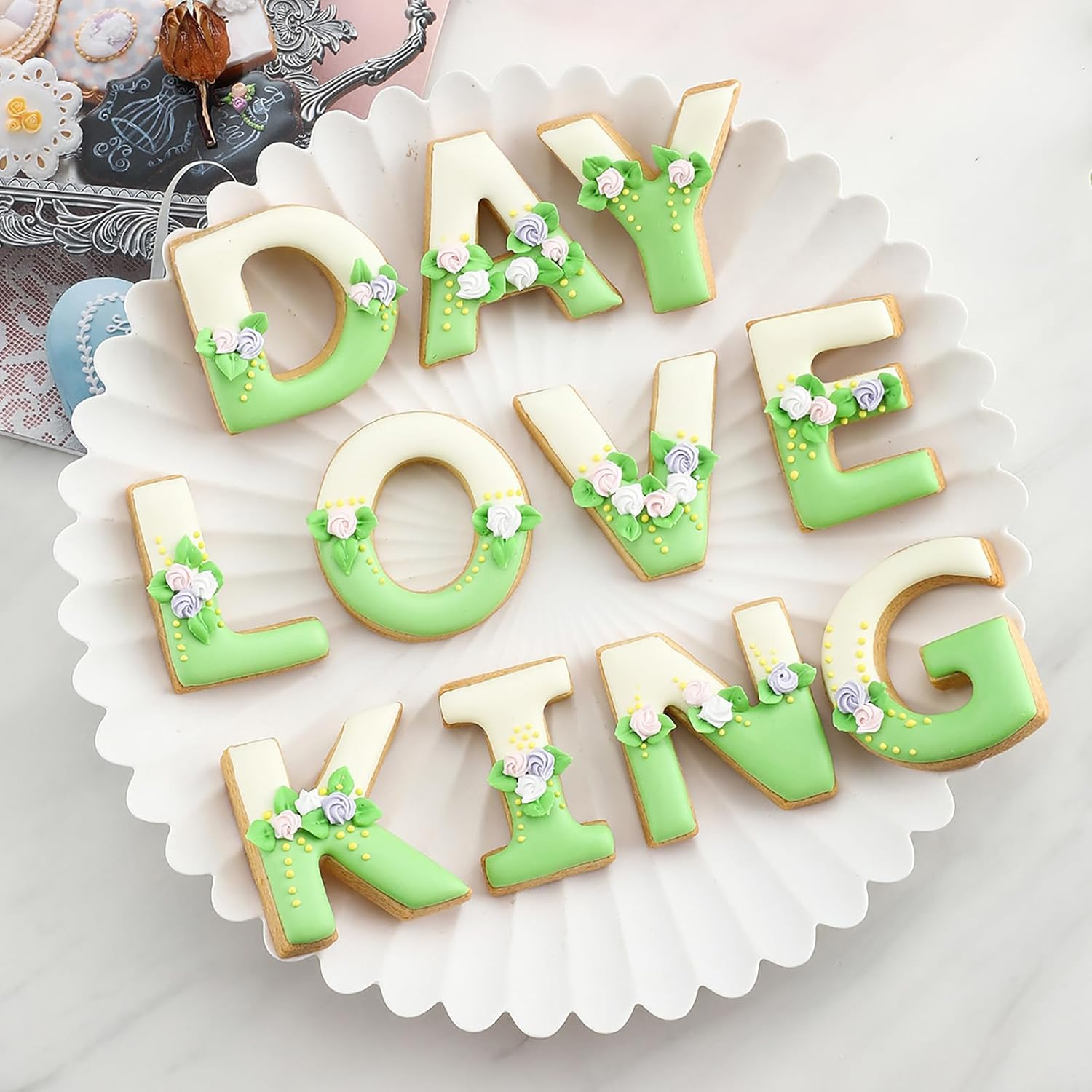 Plätzchen in Buchstabenform auf einem weißen Teller, die das Wort DAY LOVING KING bilden, verziert mit Blümchen.