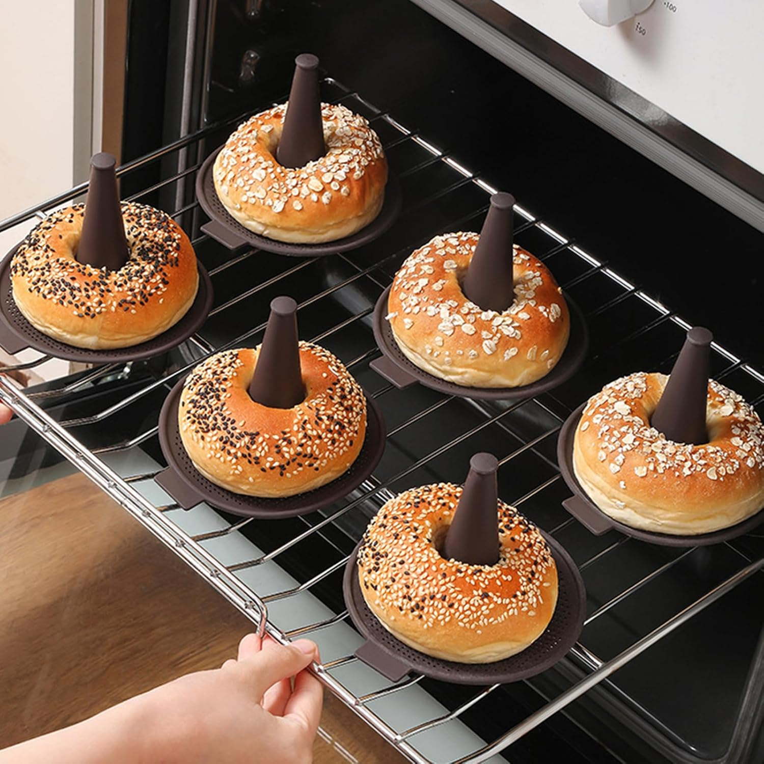 Sechs Bagels auf braunen Haltern stehen auf einem Ofenrost.