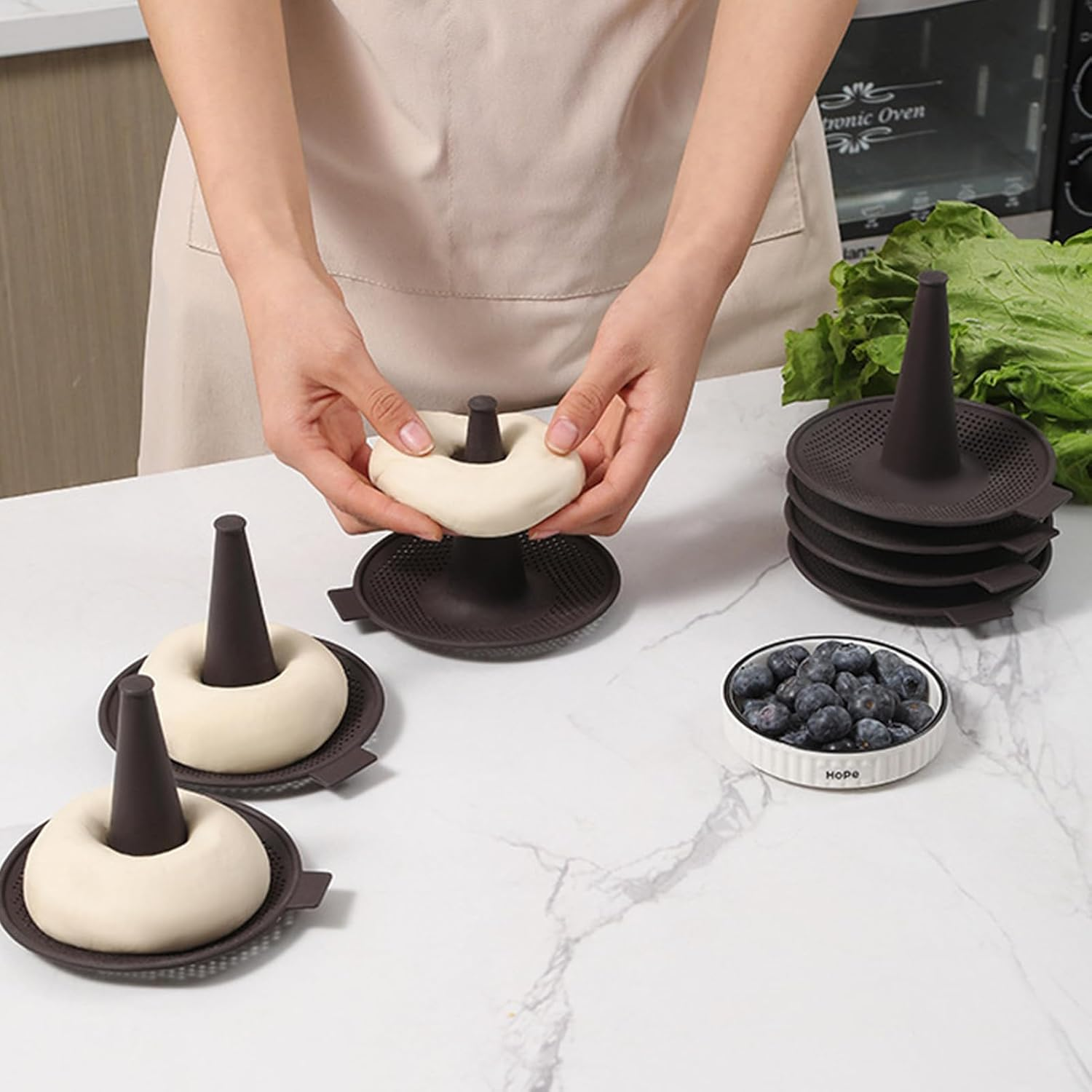 Person formt Teig um braune Kegelformen auf einer weißen Küchentheke mit Blaubeeren und Salat.