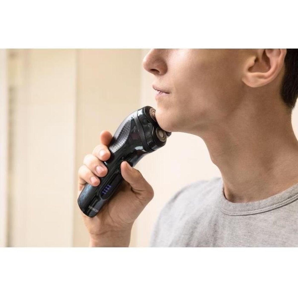 Un uomo con una camicia grigia si rade il viso con un rasoio elettrico nero.