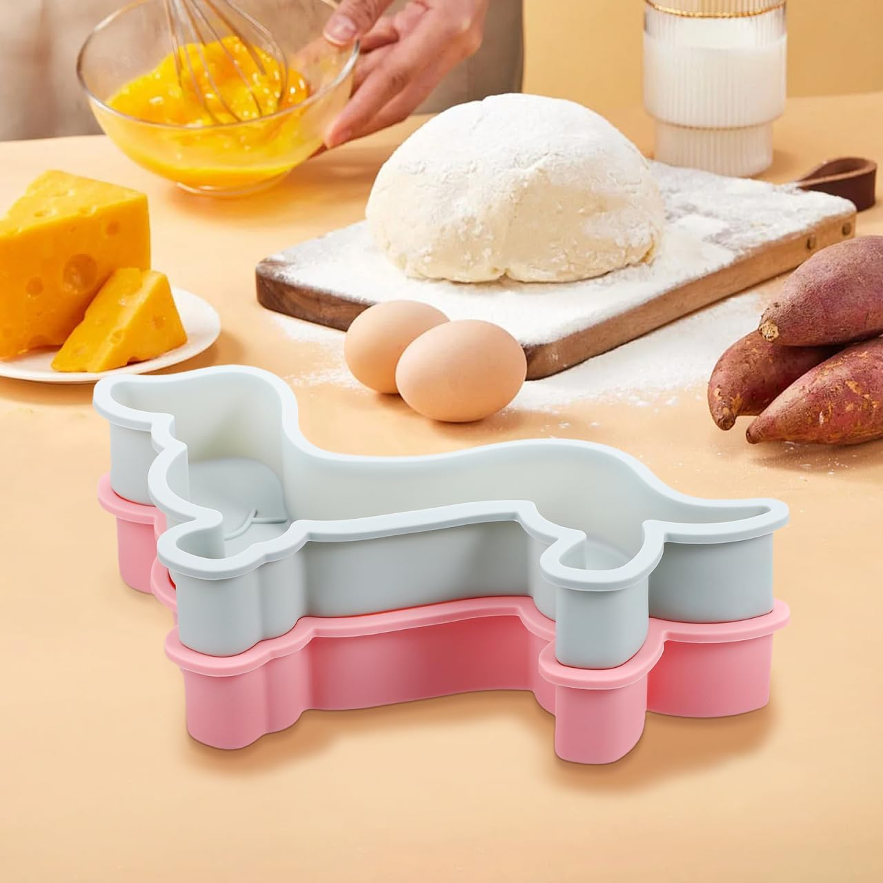 Hundeförmige Backformen im Vordergrund, Teig, Eier, Käse und Süßkartoffeln auf einem Tisch.