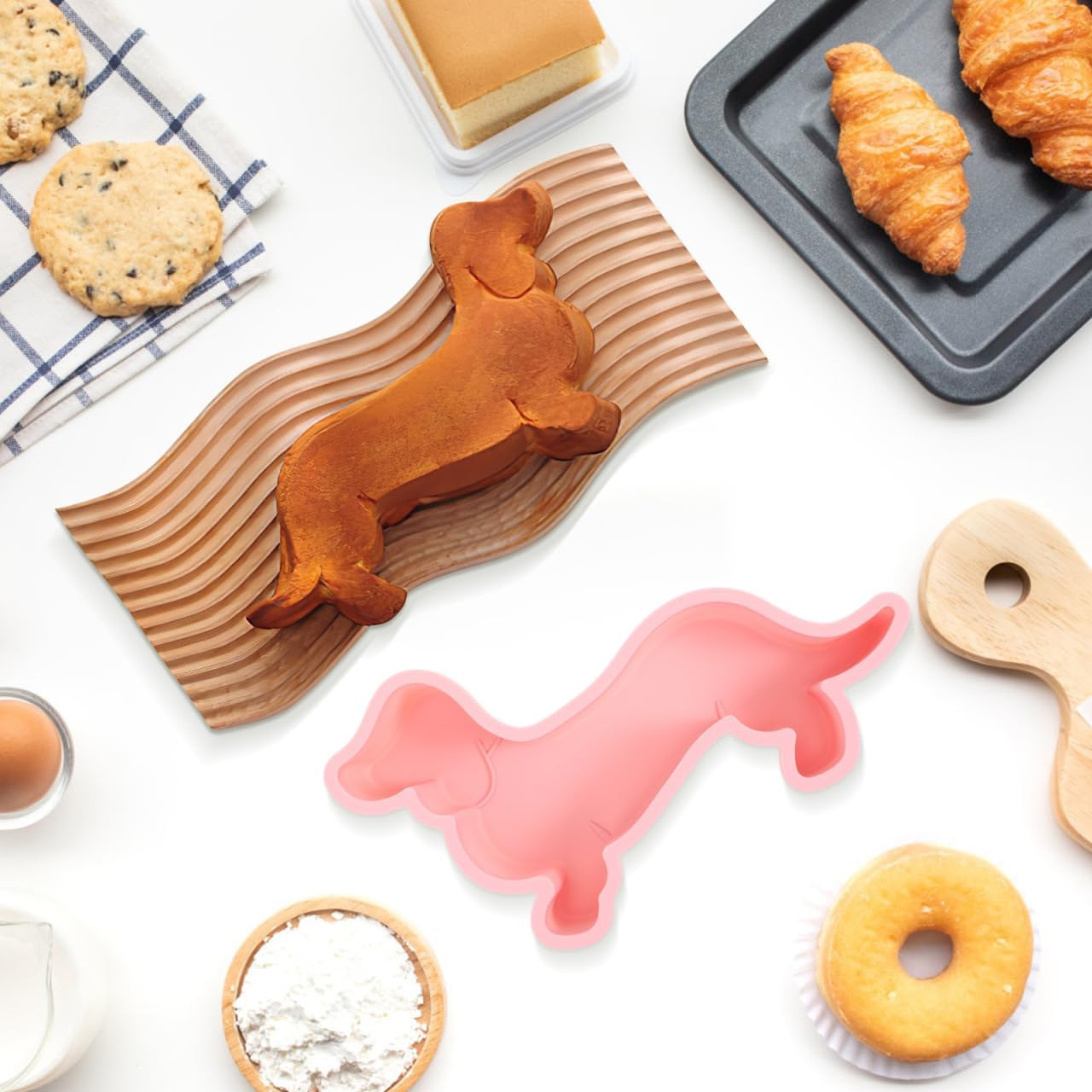 Verschiedene Backwaren, darunter ein Hundekuchen, Kekse und Croissants auf weißem Tisch.