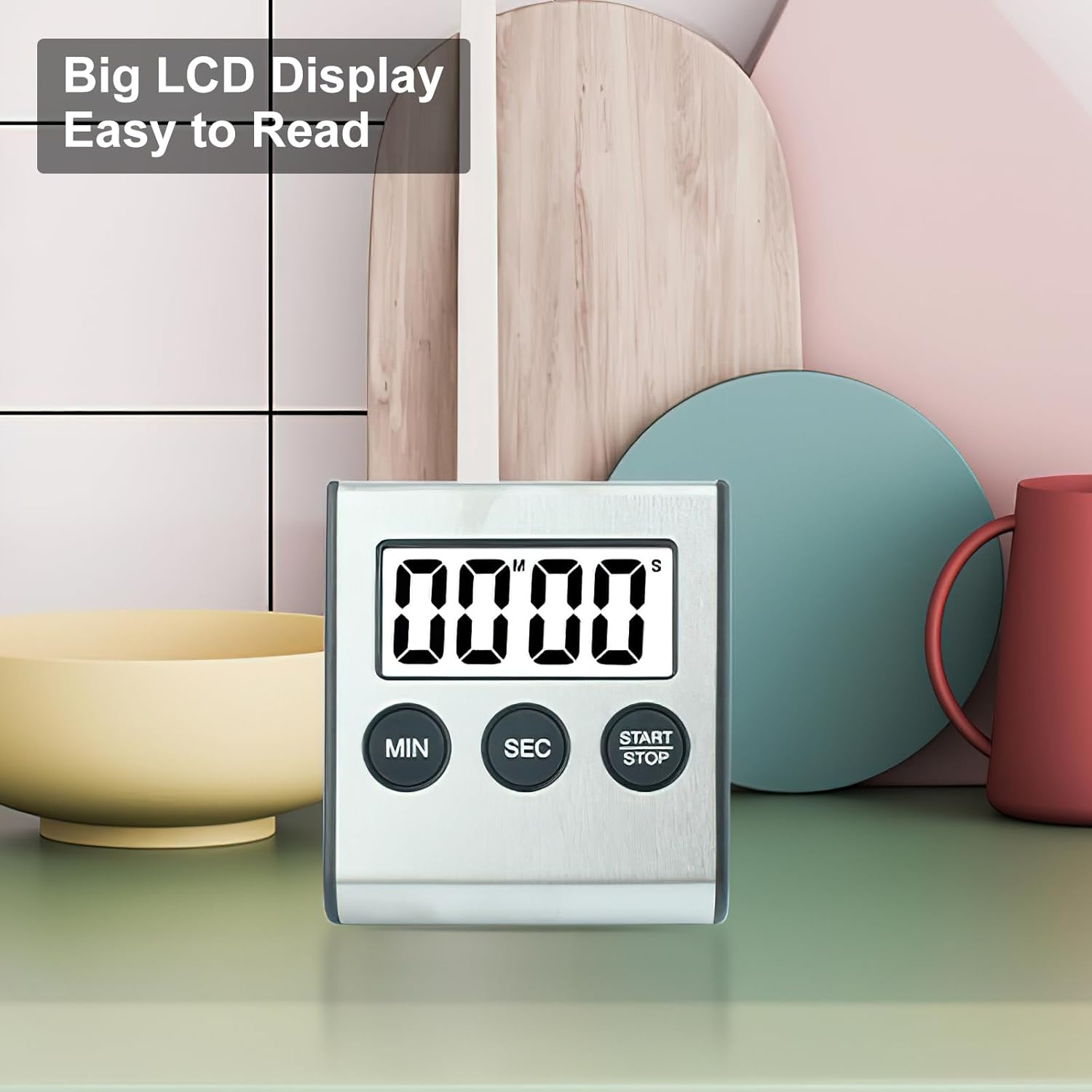 Digitale Küchenuhr mit großem LCD-Display und drei runden Tasten auf einer grünen Oberfläche vor pastellfarbenem Hintergrund.