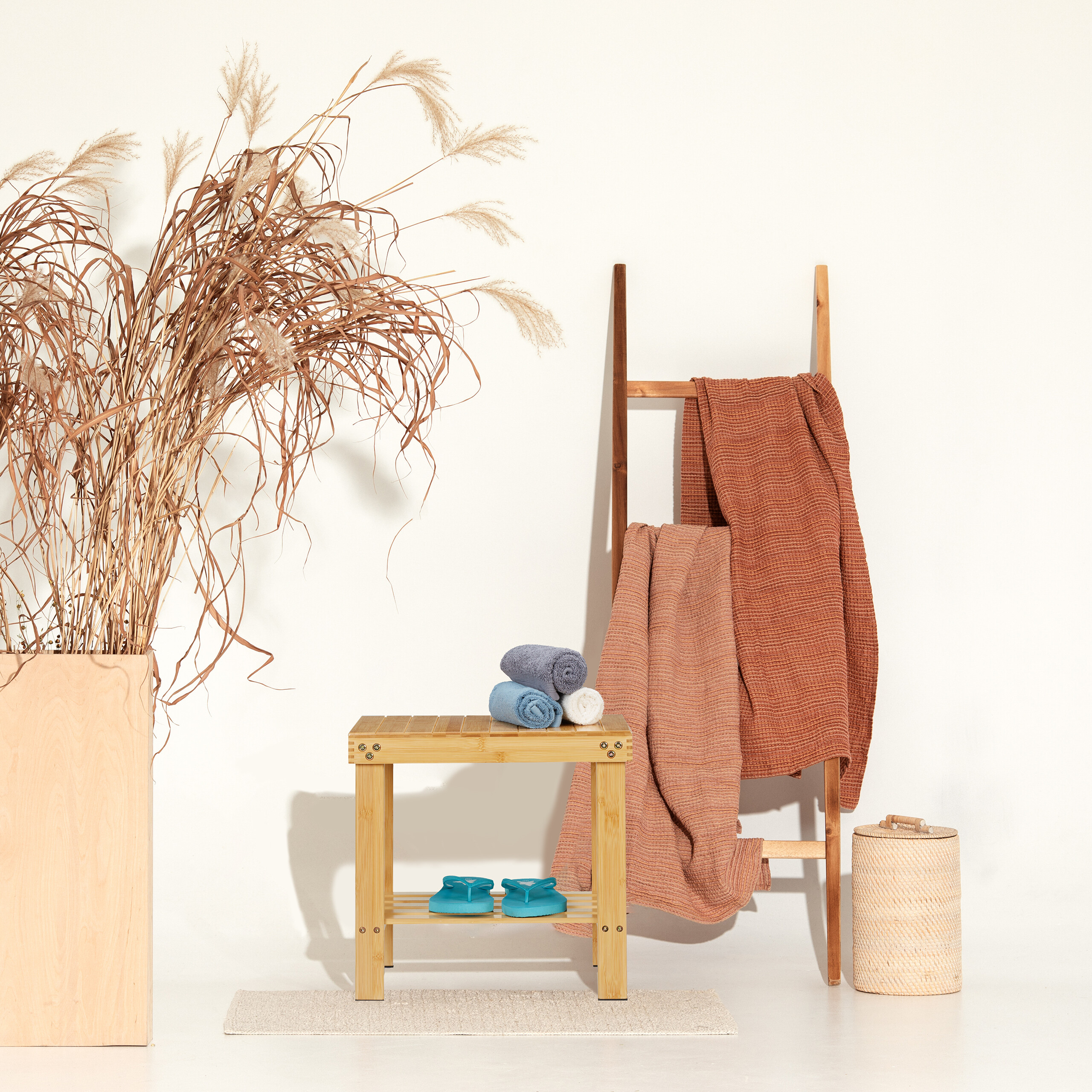 Badezimmer-Szene mit Holzhocker, Handtüchern, Leiter, getrockneten Pflanzen und einem Korb auf weißem Hintergrund.
