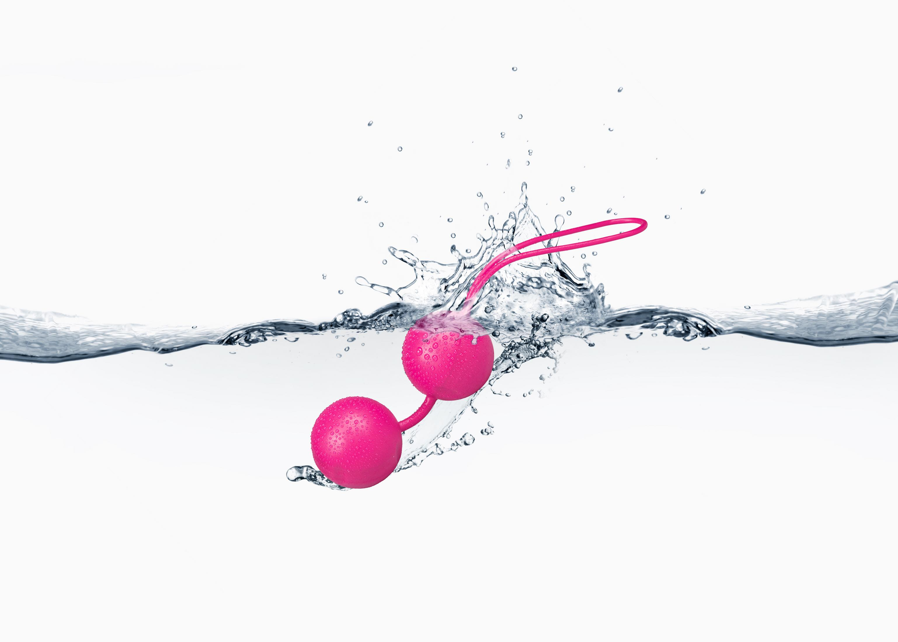 Zwei pinke Liebeskugeln tauchen in Wasser ein und erzeugen Spritzer.