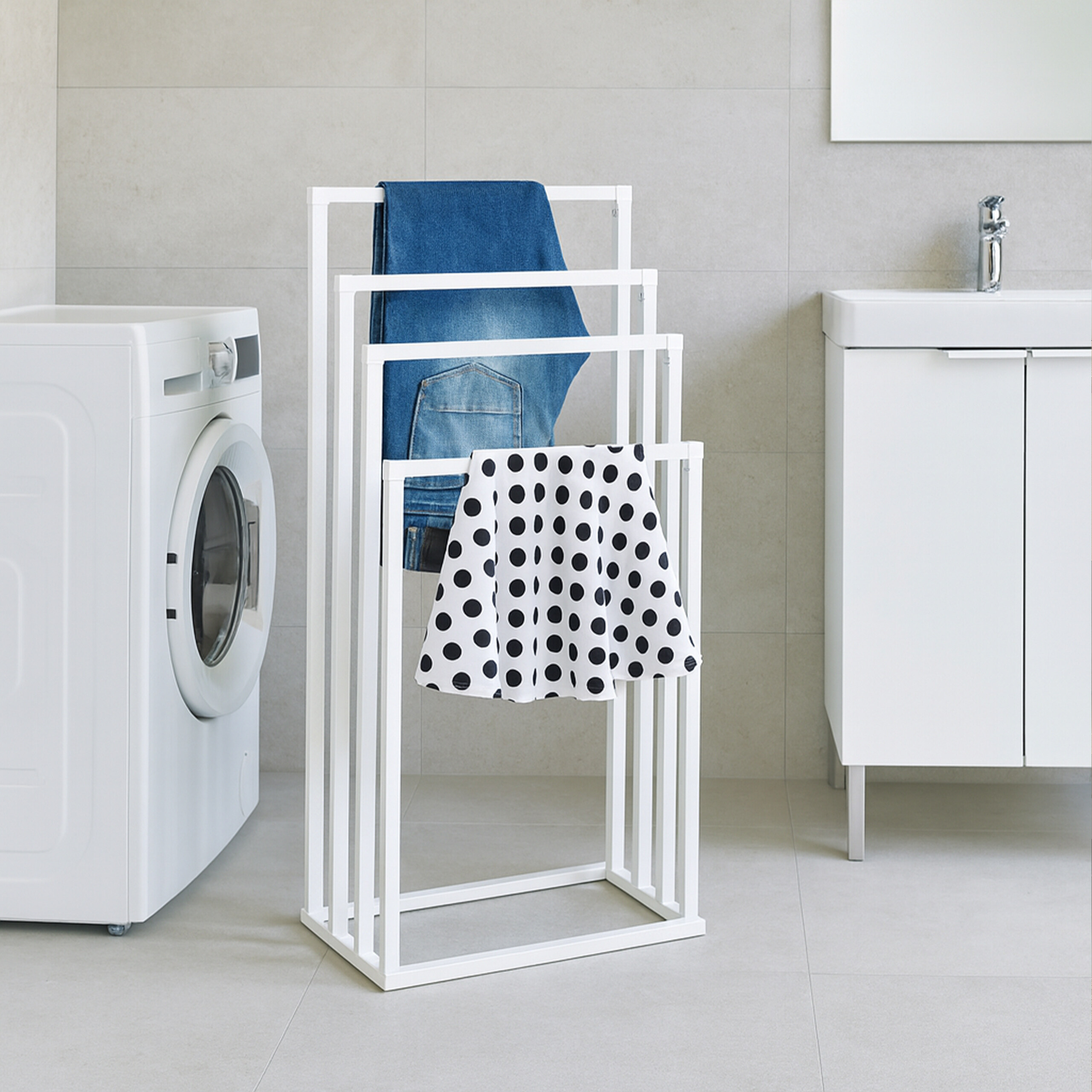 Ein weißer Handtuchhalter steht im Badezimmer mit blauen Jeans und einem schwarz-weiß getupften Tuch.
