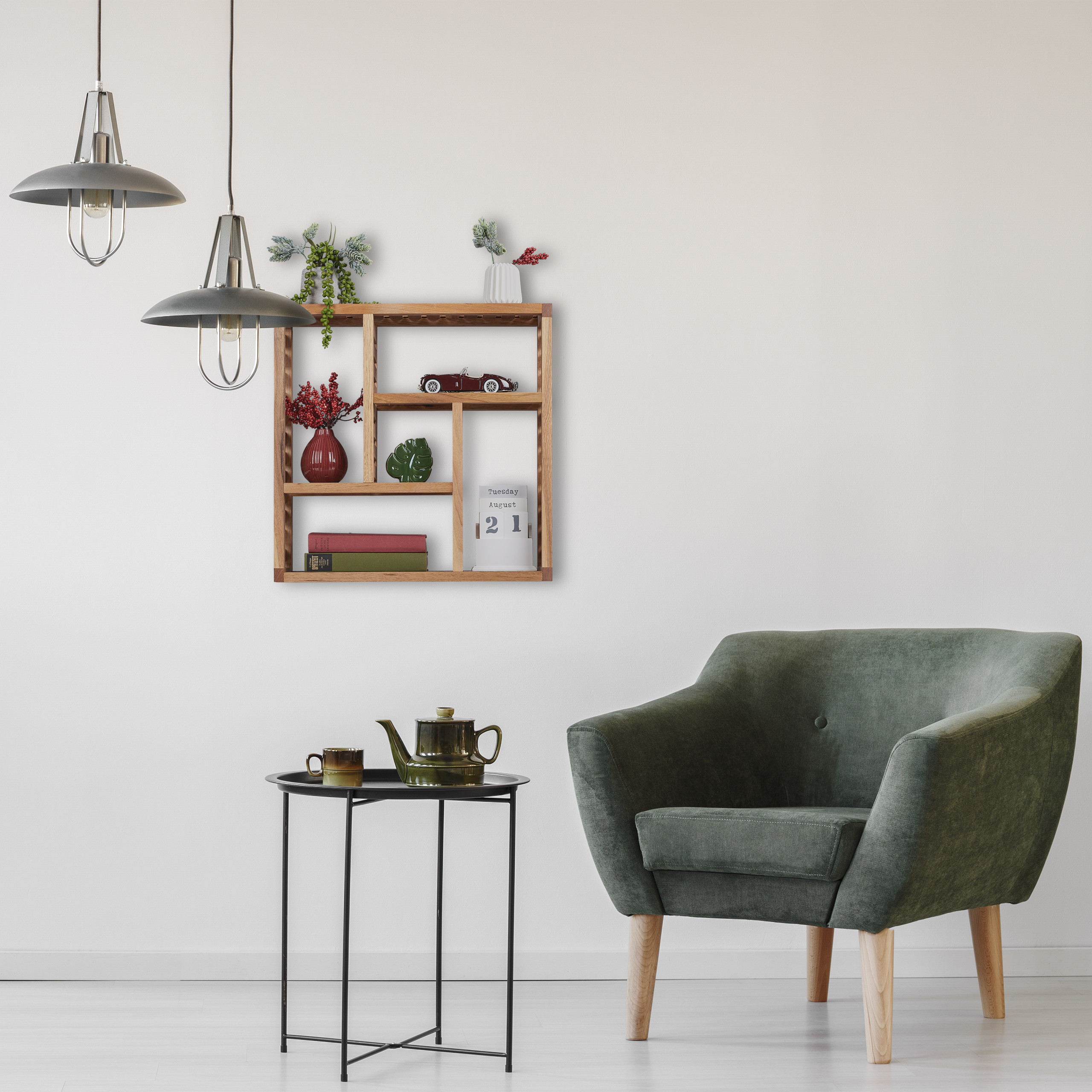Ein grüner Sessel und ein kleiner Tisch mit Teekanne und Tasse, daneben Hängelampen und ein Holzregal an der weißen Wand.