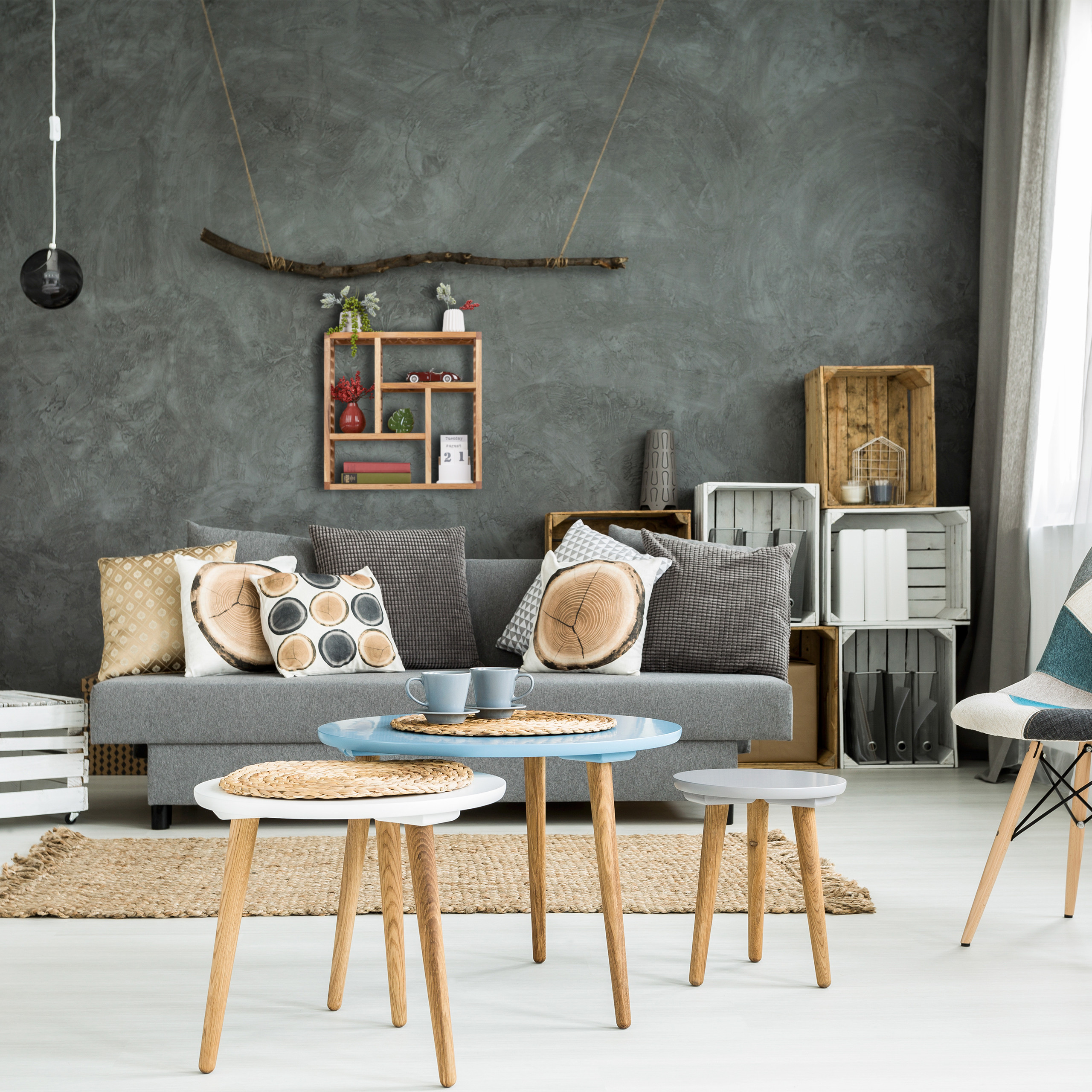 Gemütliches Wohnzimmer mit grauem Sofa, runden Holztischen und Wandregalen an grauer Wand.