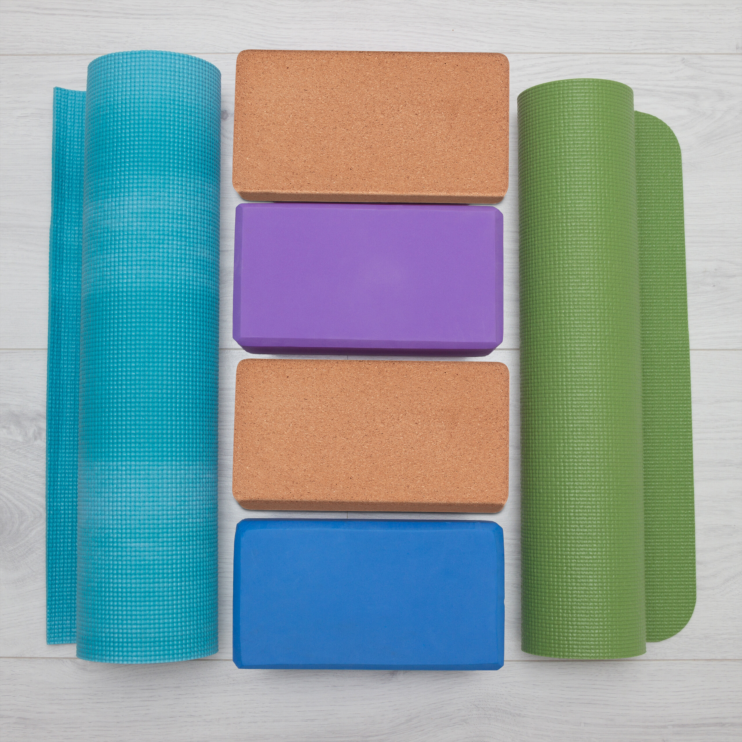 Yoga-Zubehör mit einer blauen Matte, zwei Korkblöcken, einem lila Block, einem blauen Block und einer grünen Matte.