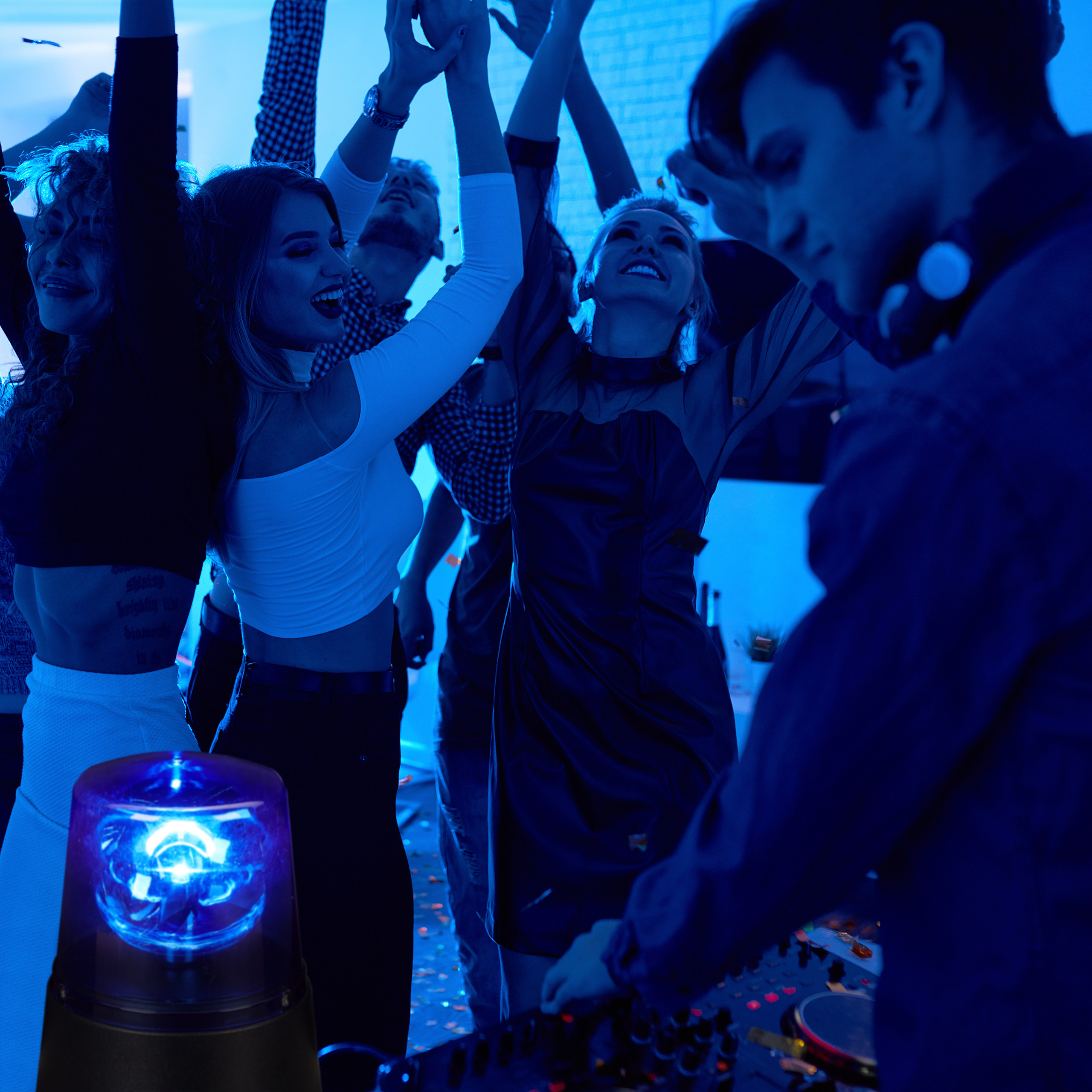 Menschen feiern bei blauem Licht in einem Club, im Vordergrund legt ein DJ auf.
