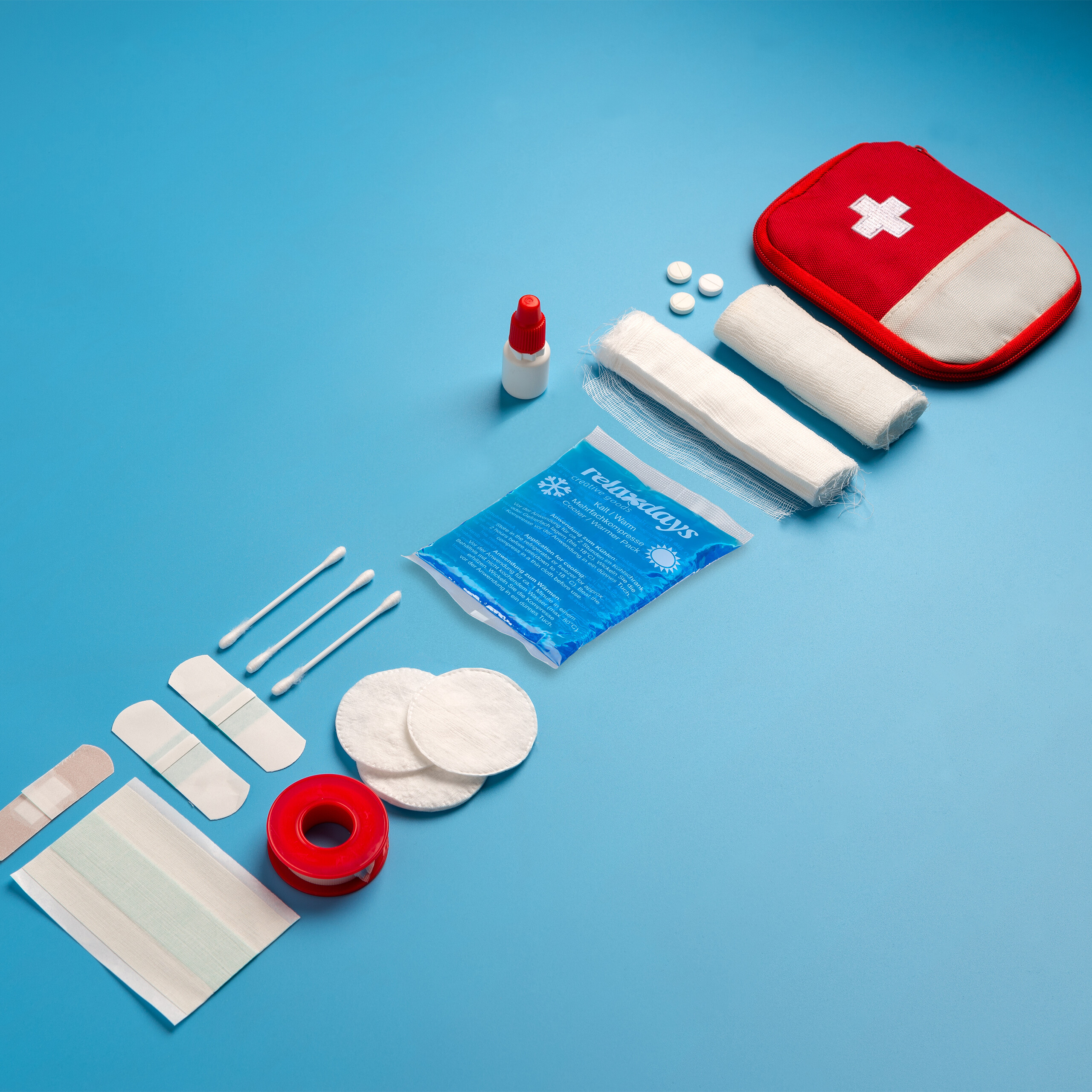 Ein rotes Erste-Hilfe-Set mit medizinischen Utensilien, Pflastern und Bandagen ordentlich auf blauem Hintergrund angeordnet.