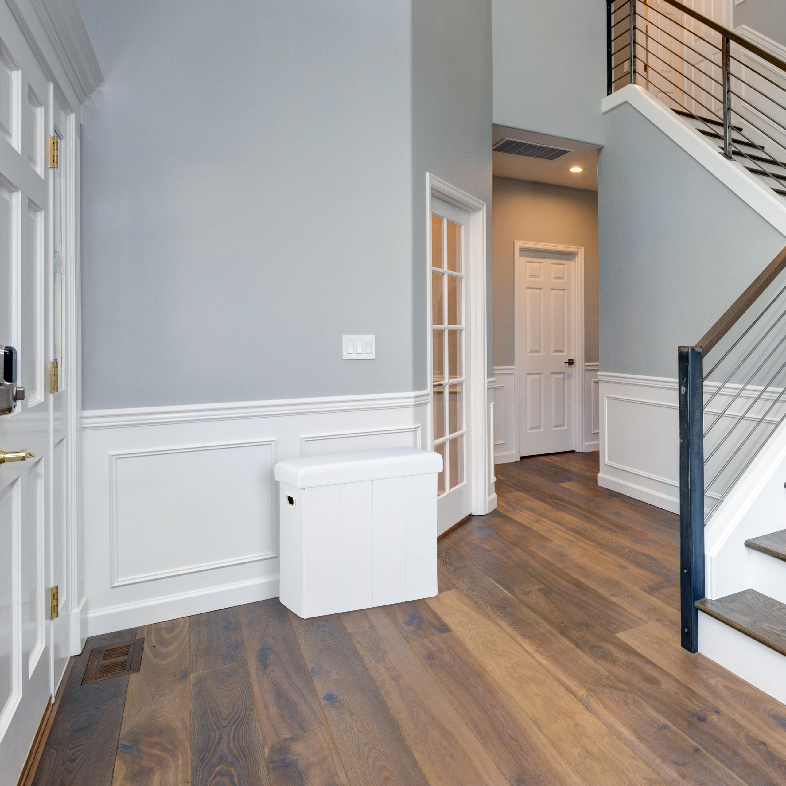 Ein heller Flur mit Holzböden, grau-weißen Wänden, weißer Holztäfelung und einer Treppe mit Metallgeländer.