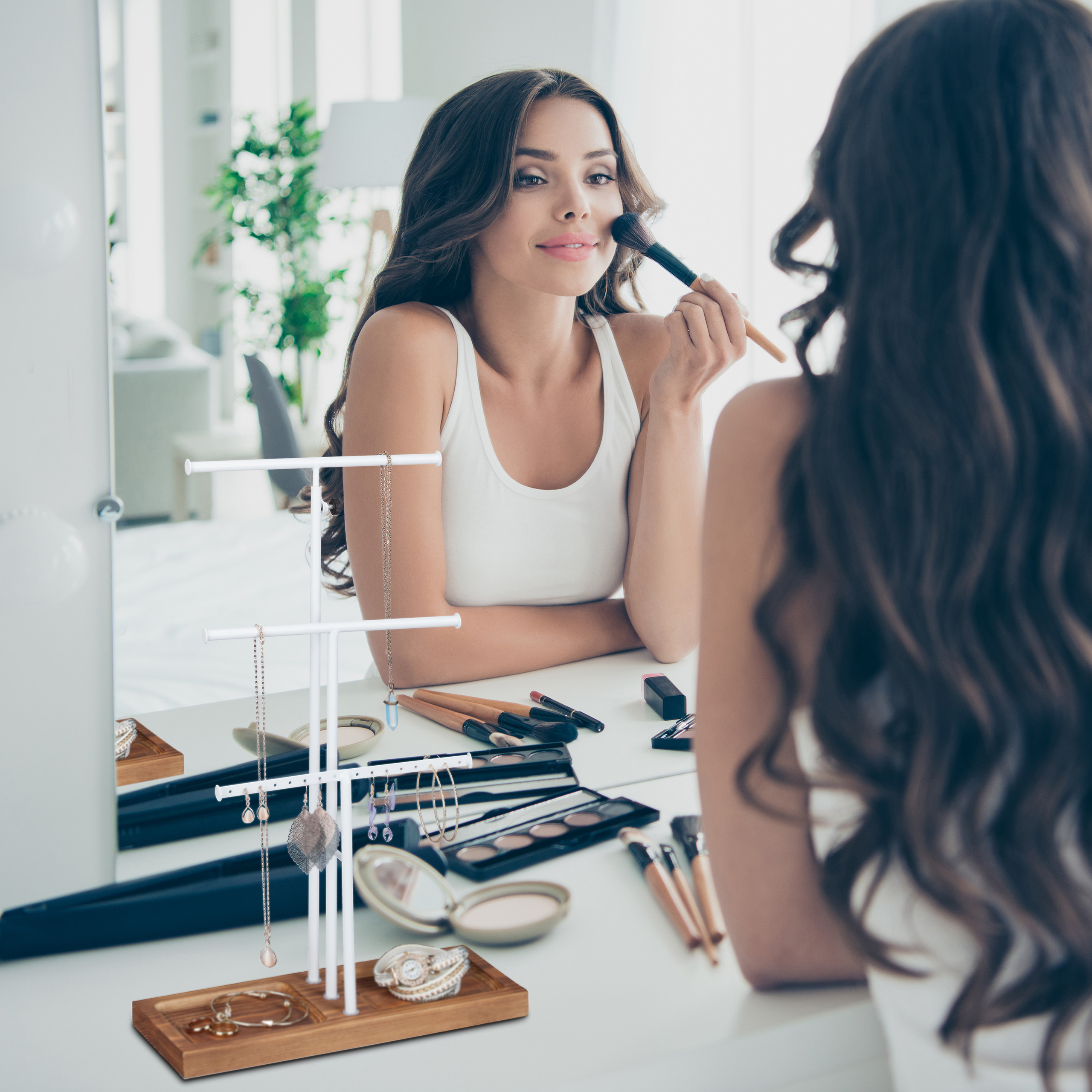 Eine Frau im weißen Top trägt vor einem Spiegel Make-up auf.