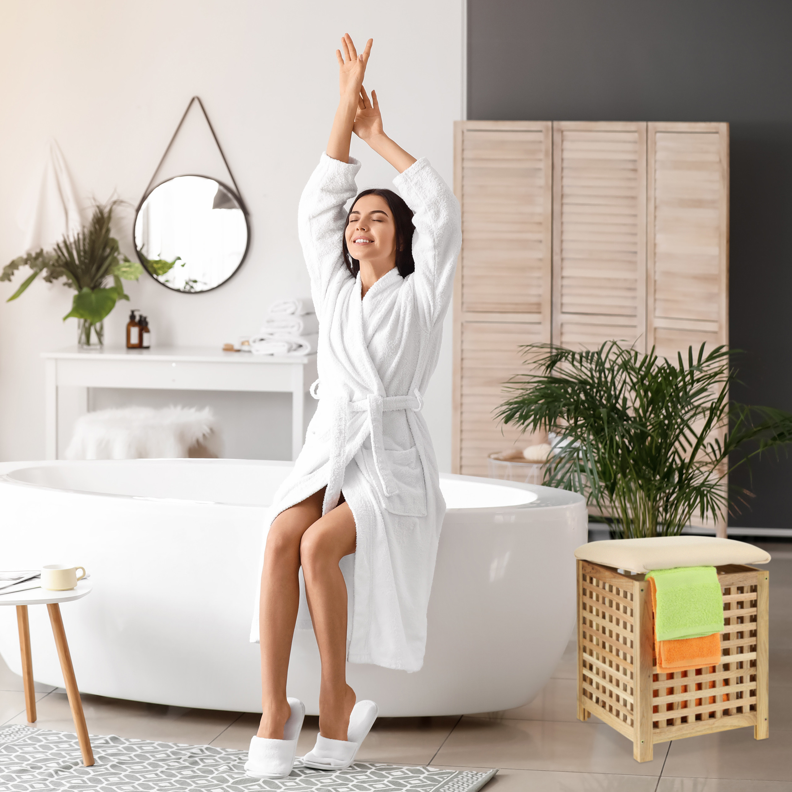 Eine Frau im weißen Bademantel sitzt auf einer Badewanne und streckt sich in einem hellen Badezimmer.