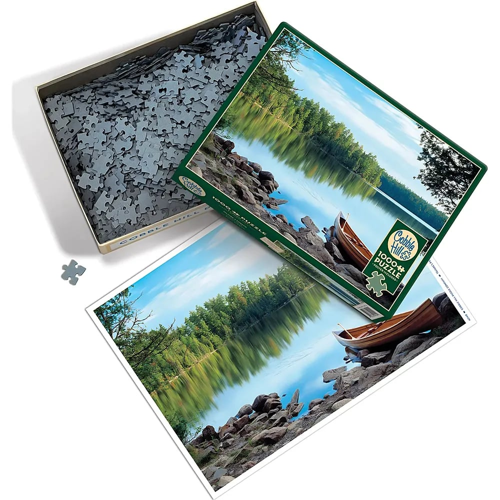 Eine offene Puzzle-Schachtel mit Teilen, neben einem Deckel und einem Poster mit einem ruhigen See.