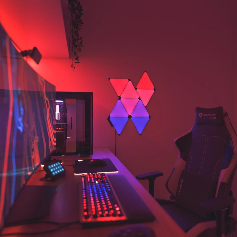 Podświetlane biurko dla gracza z monitorem, klawiaturą RGB, myszką, komputerem i fotelem w czerwonym świetle.