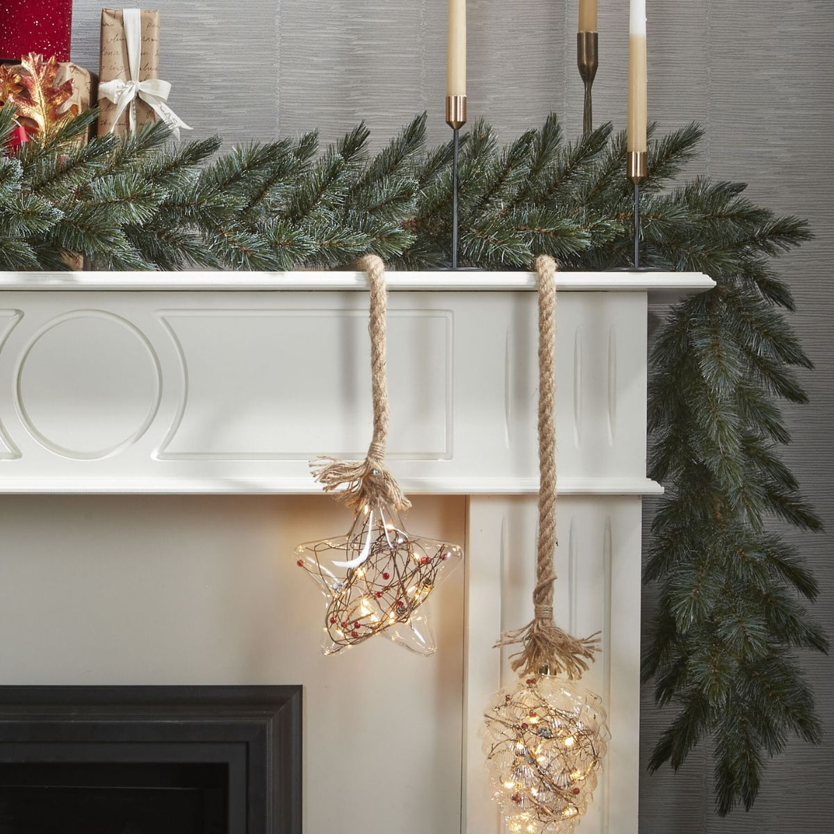 Guirlande de Noël sur manteau blanc avec étoile et boule lumineuses suspendues, bougies et cadeaux.