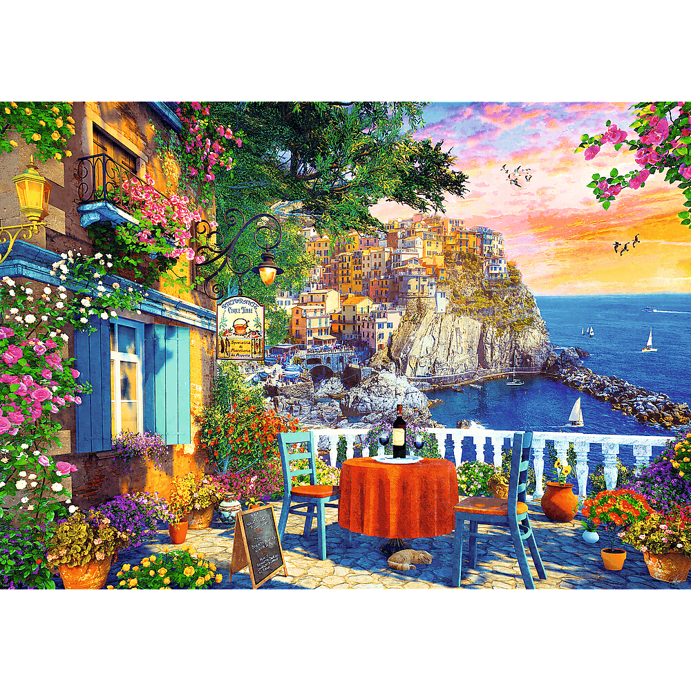 Eine bunte Küstenterrasse mit Blick auf ein Kaffeedorf bei Sonnenuntergang, Tisch, Stühlen und Blumen.
