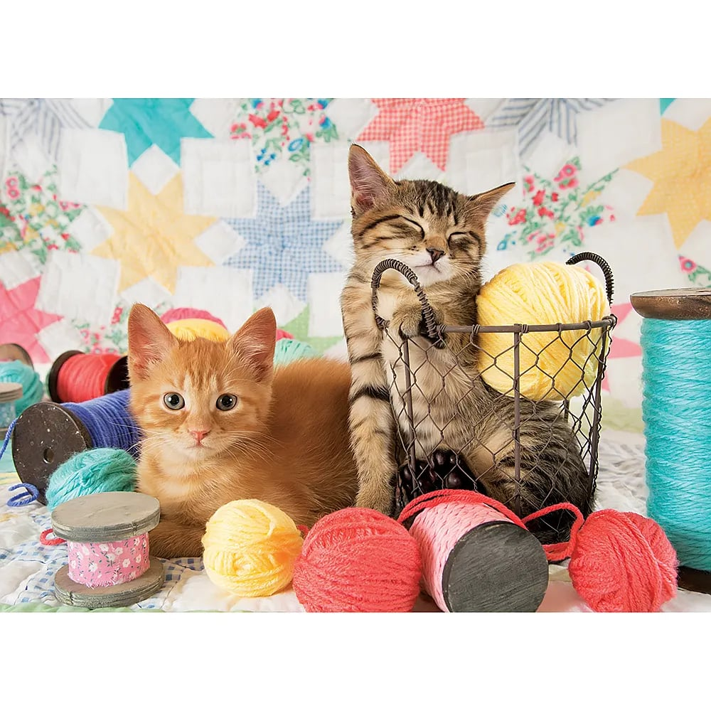Zwei süße Kätzchen mit bunten Garnknäueln und Spulen vor einem Quilt-Hintergrund.