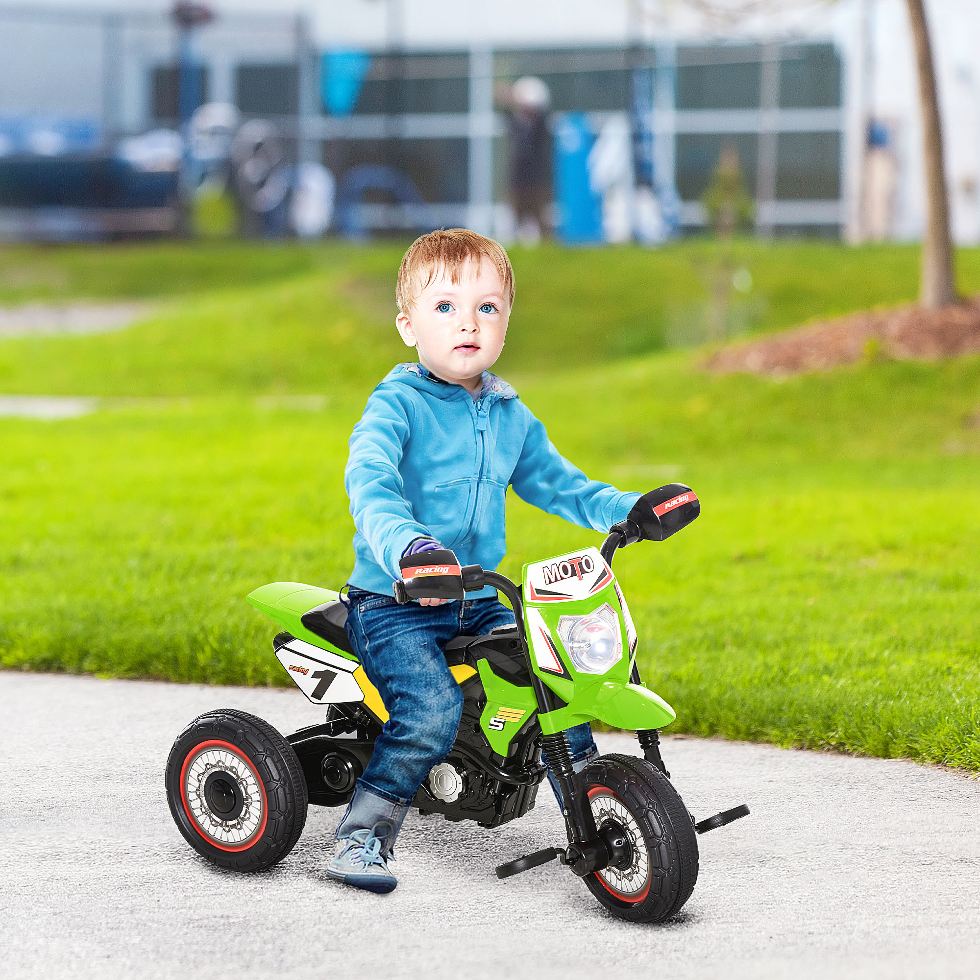 Bambino con giacca blu siede all'aperto su un triciclo a moto verde.
