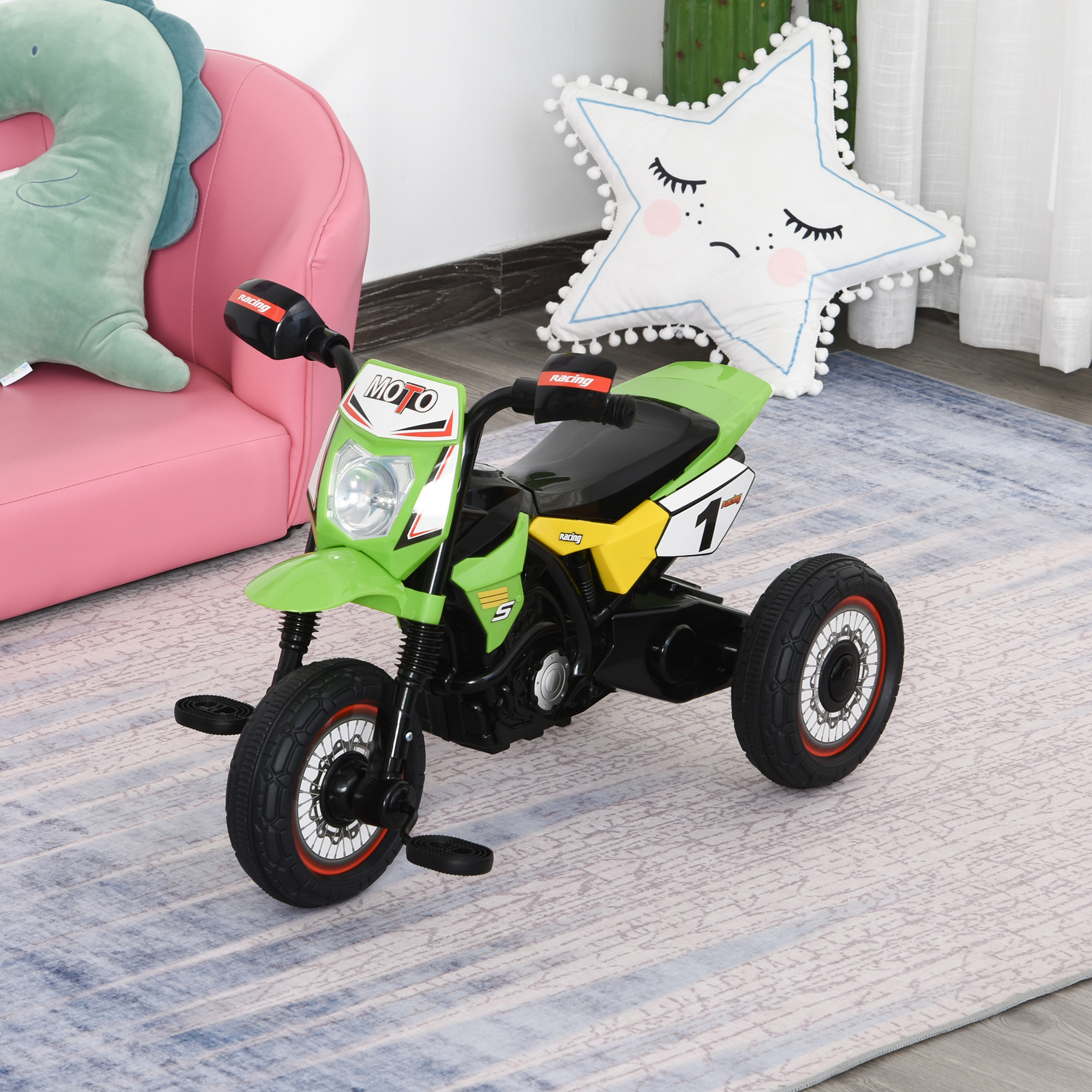 Un triciclo giocattolo a forma di moto verde, giallo e nero si trova su un tappeto davanti a un divano rosa e un cuscino a stella.