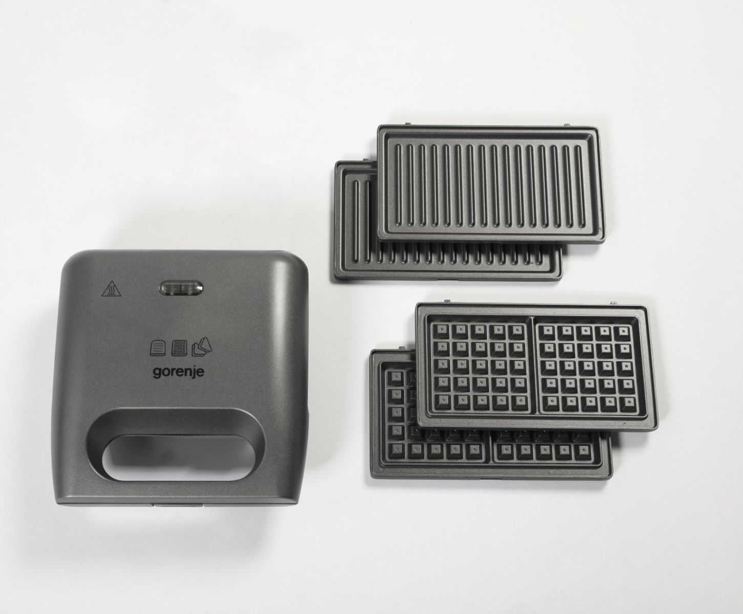Una piastra per panini Gorenje grigia accanto a due piastre grill e due piastre per waffle su sfondo bianco.