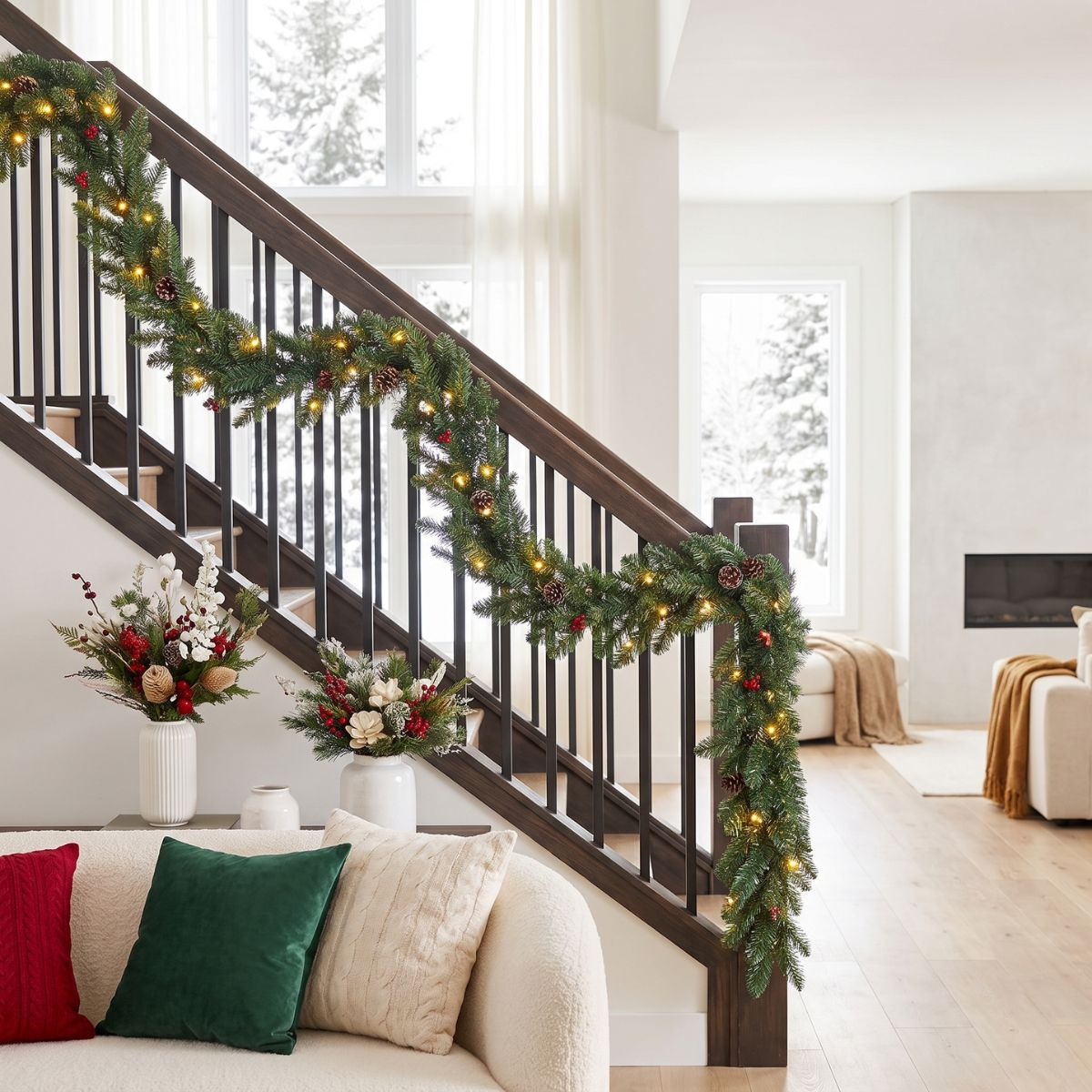 Eine grüne Weihnachtsgirlande mit Lichtern und Tannenzapfen dekoriert die Treppe in einem hellen Wohnzimmer.