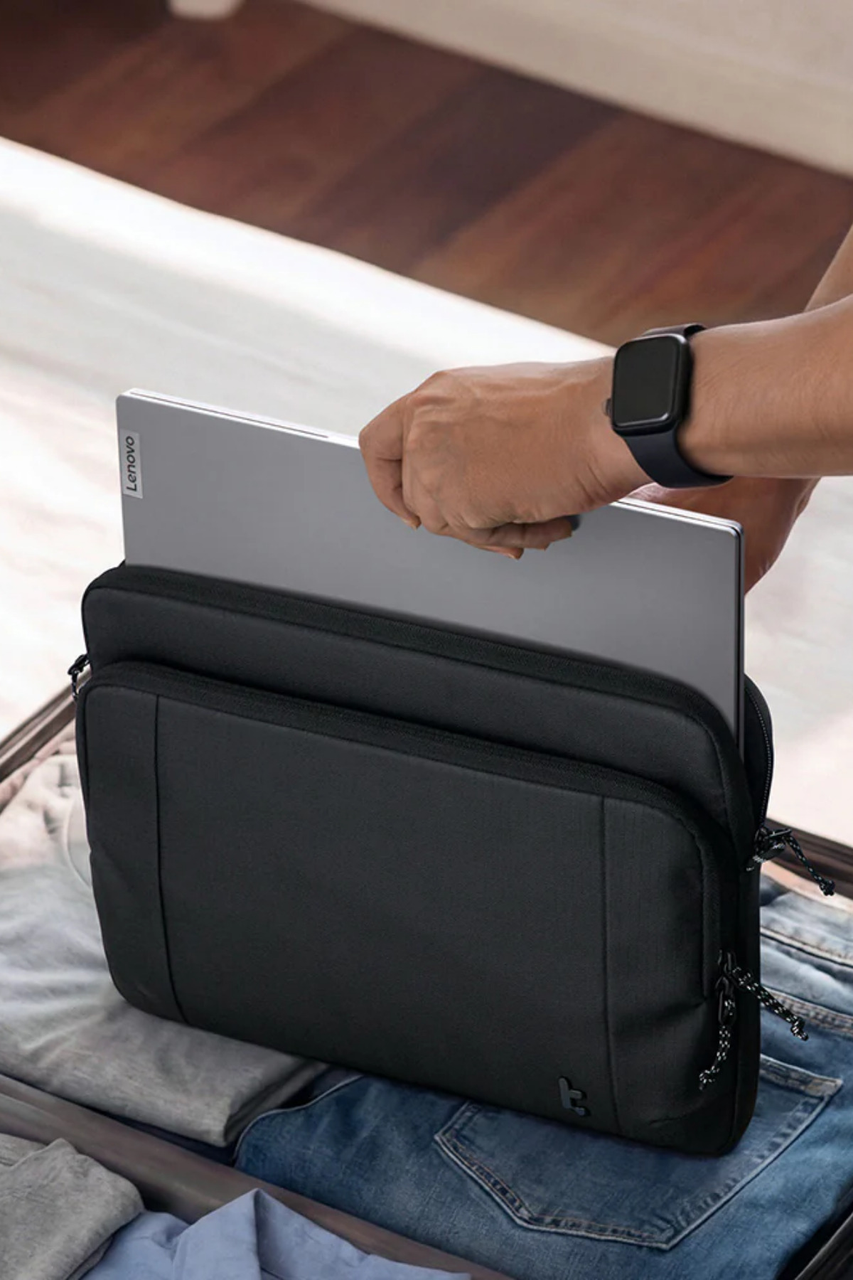 Bir kişi, valizin içindeki siyah bir dizüstü bilgisayar kılıfına gri bir Lenovo dizüstü bilgisayar yerleştiriyor.