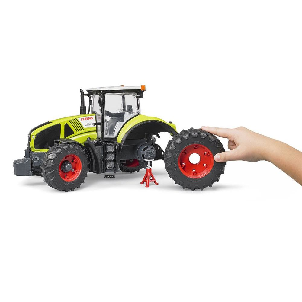 Ein Kind wechselt das Hinterrad eines grünen Claas-Spielzeugtraktors auf einem Ständer vor weißem Hintergrund.
