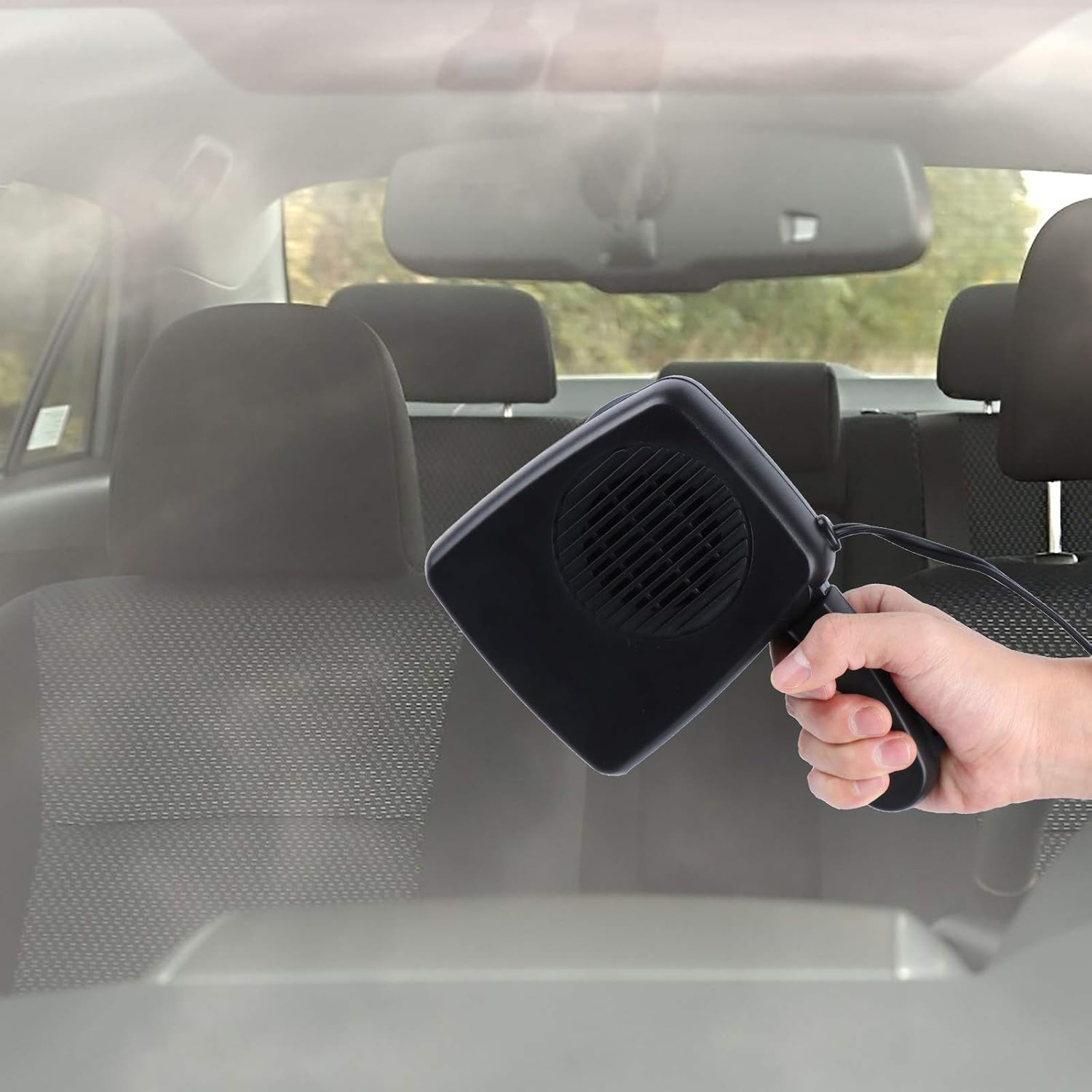 Eine Hand hält einen kleinen schwarzen Autoheizlüfter im Innenraum eines Autos.