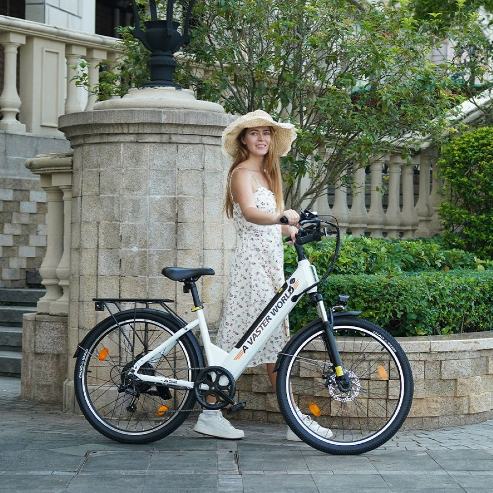 Una donna sorridente con cappello di paglia e abito floreale è accanto a una bici elettrica bianca.
