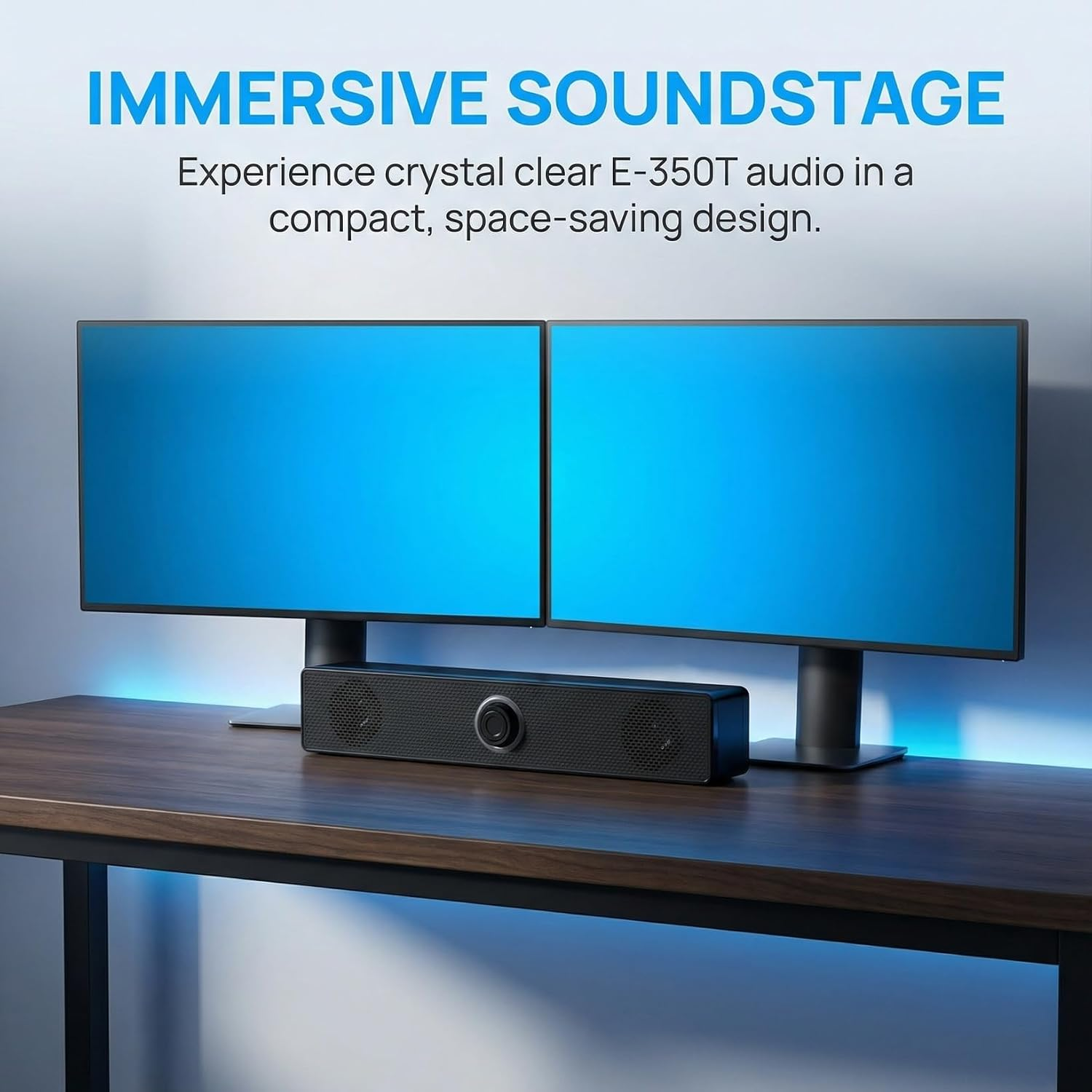 Eine lange schwarze Soundbar steht auf einem Holztisch unter zwei Computermonitoren mit blauem Bildschirm.