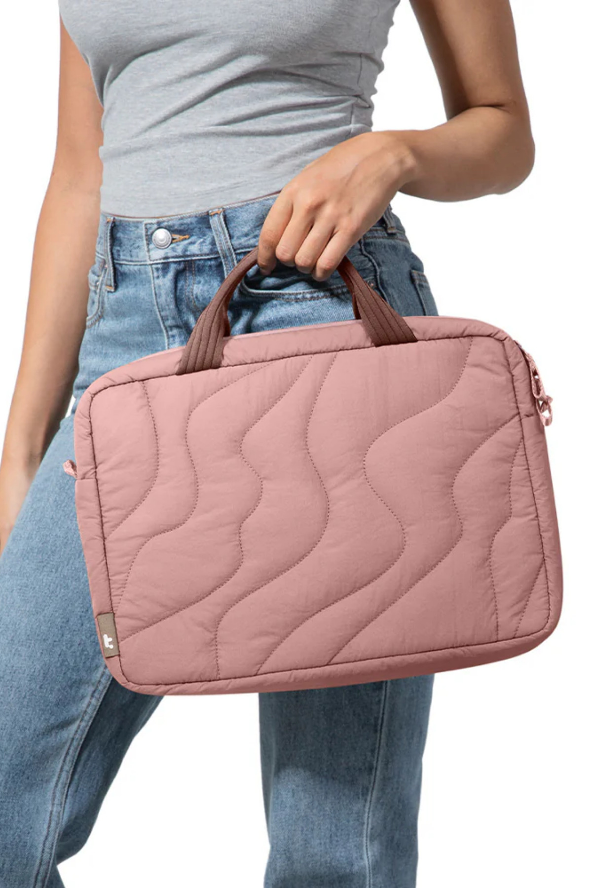 Kot pantolon ve gri üst giyen bir kadın, kahverengi saplı pembe kapitone laptop çantası tutuyor.