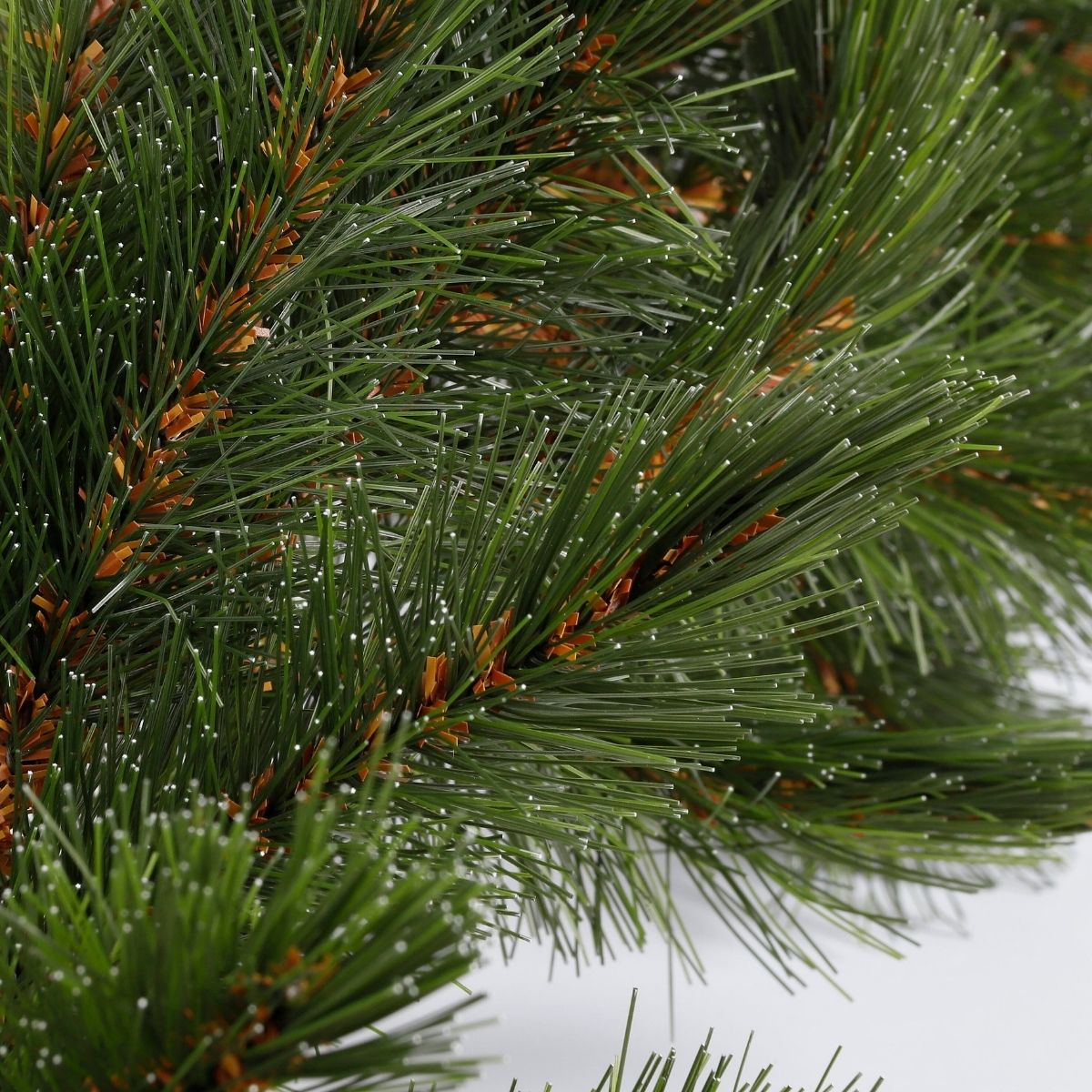 Gros plan de branches de pin vertes artificielles avec des tiges brunes sur fond blanc.