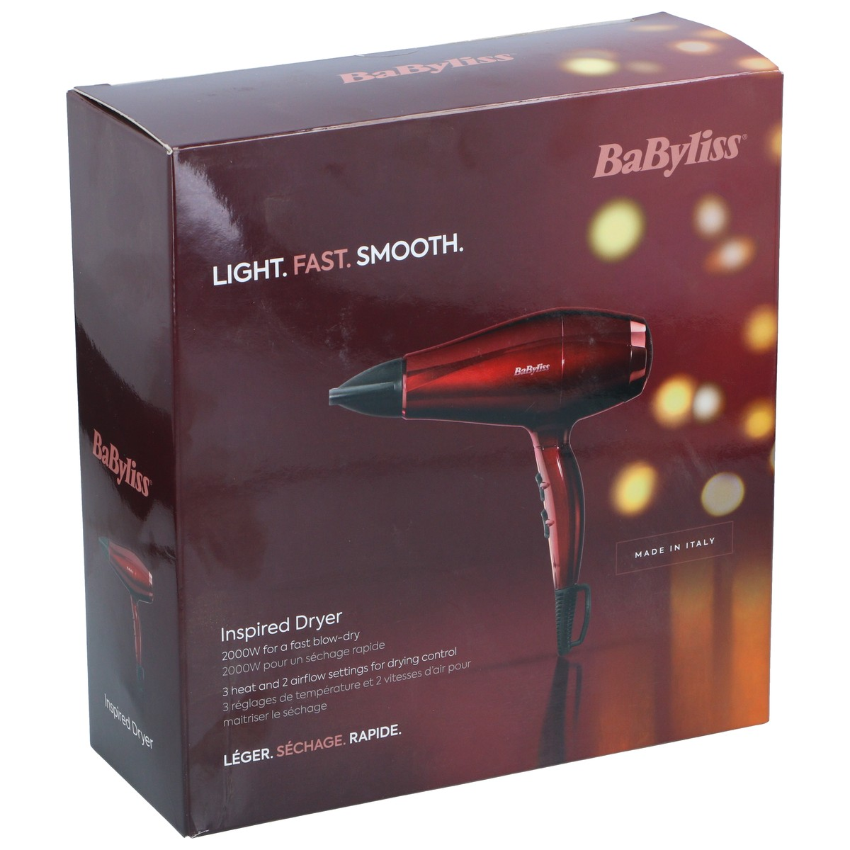 Eine bordeauxrote BaByliss Haartrockner Verpackung mit Produktbild und Texten vor einem unscharfen Lichterhintergrund.