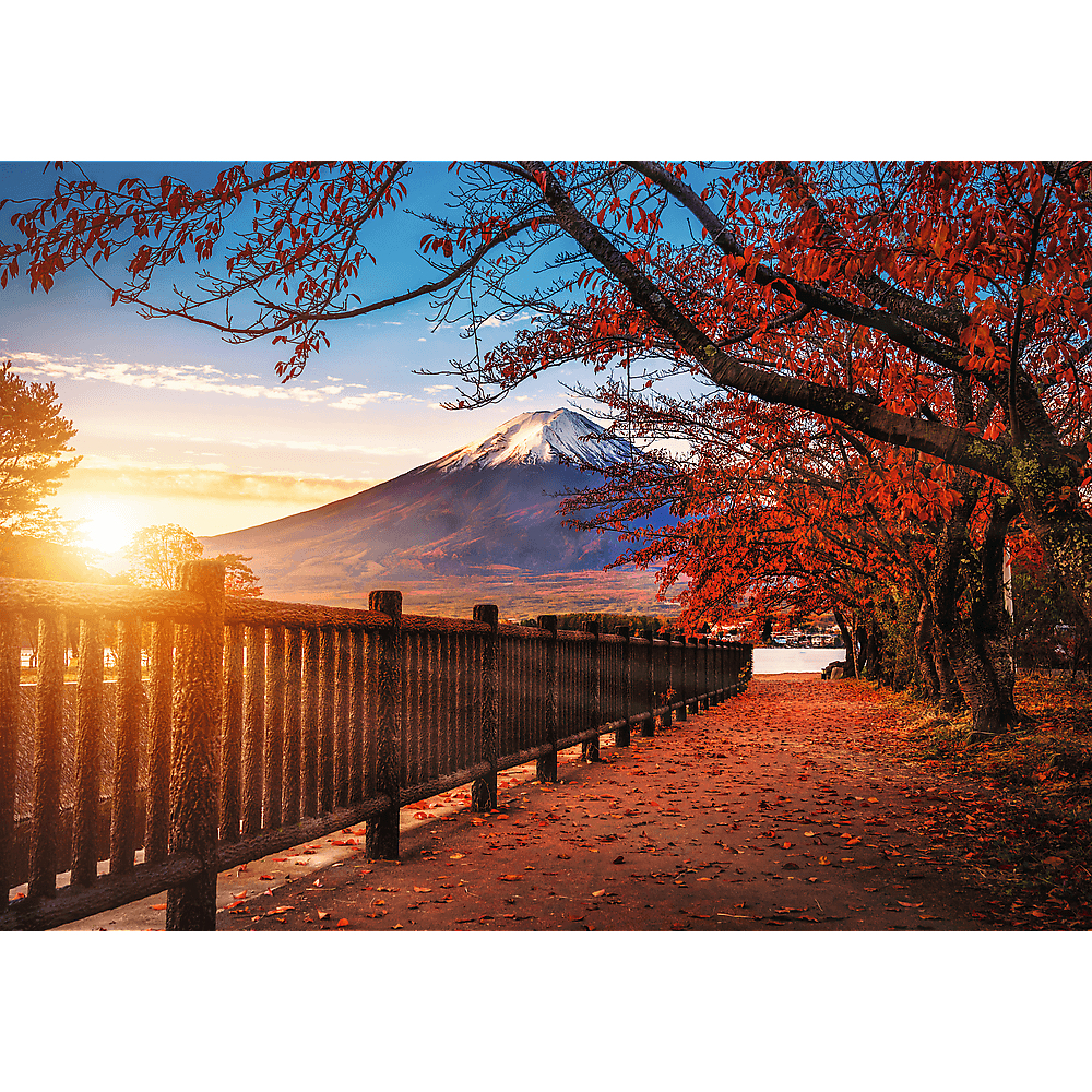 Ein malerischer Weg mit Herbstlaub, einem Holzzaun und dem Berg Fuji im Hintergrund bei Sonnenaufgang.