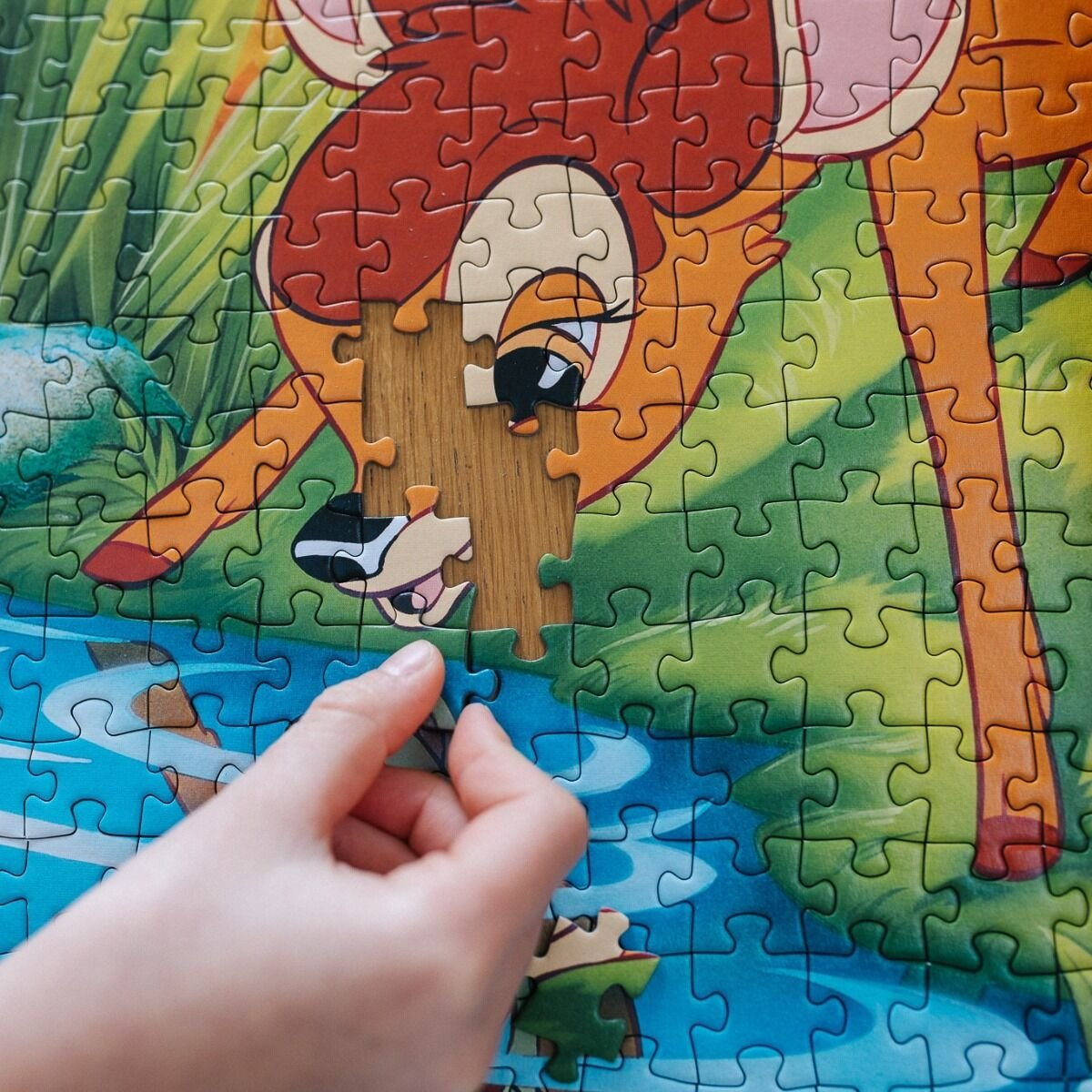 Eine Hand setzt ein letztes Puzzleteil in ein Bambi-Motiv ein.