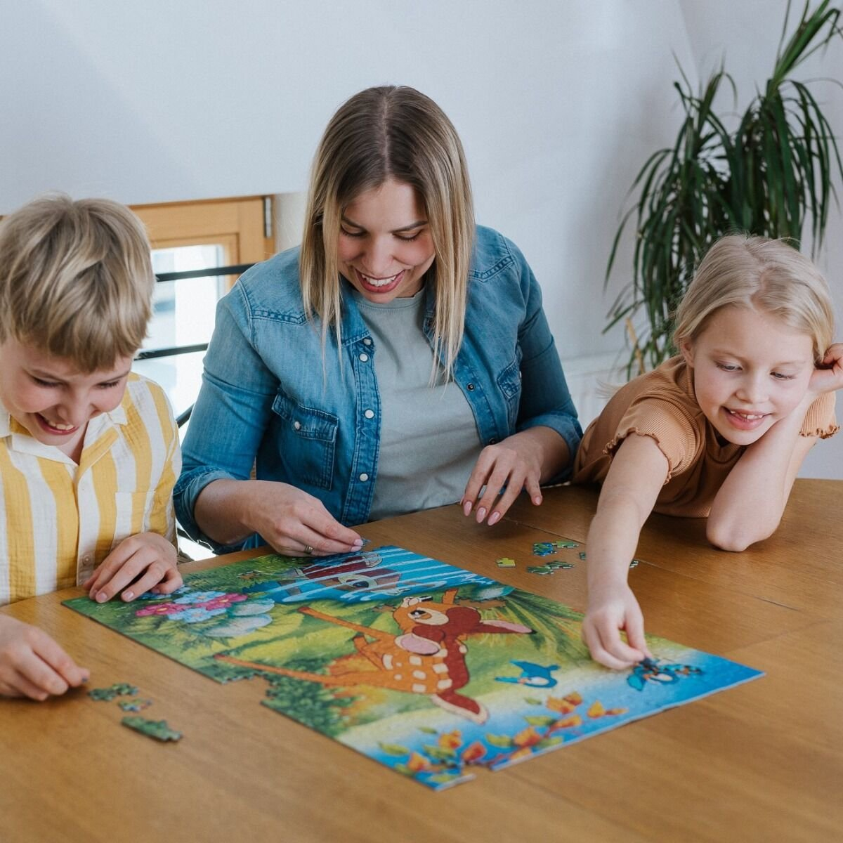 Eine Frau und zwei Kinder sitzen an einem Holztisch und machen zusammen ein buntes Tierpuzzle.