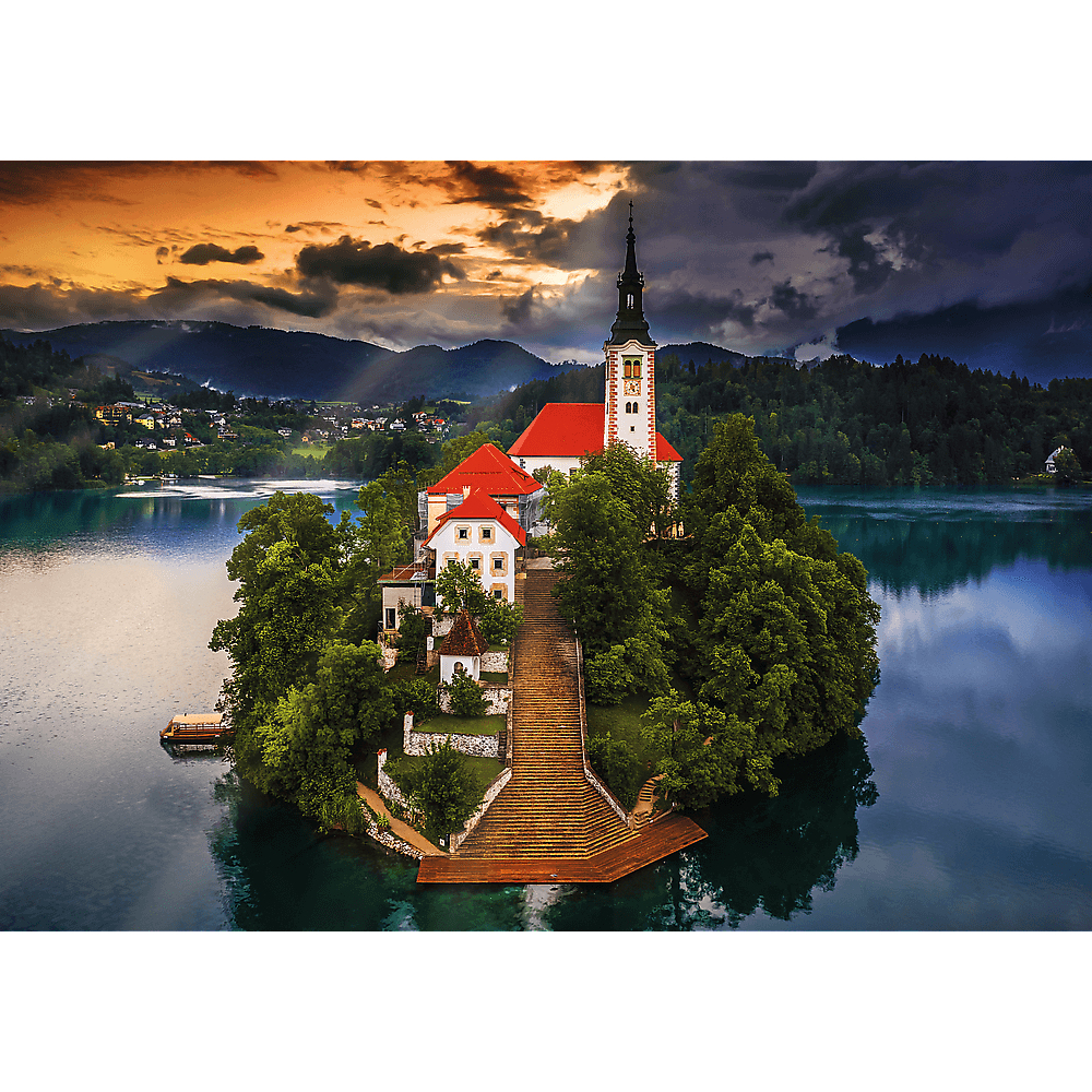 Isla escénica con iglesia y larga escalinata en el medio de un lago tranquilo bajo un cielo de atardecer.